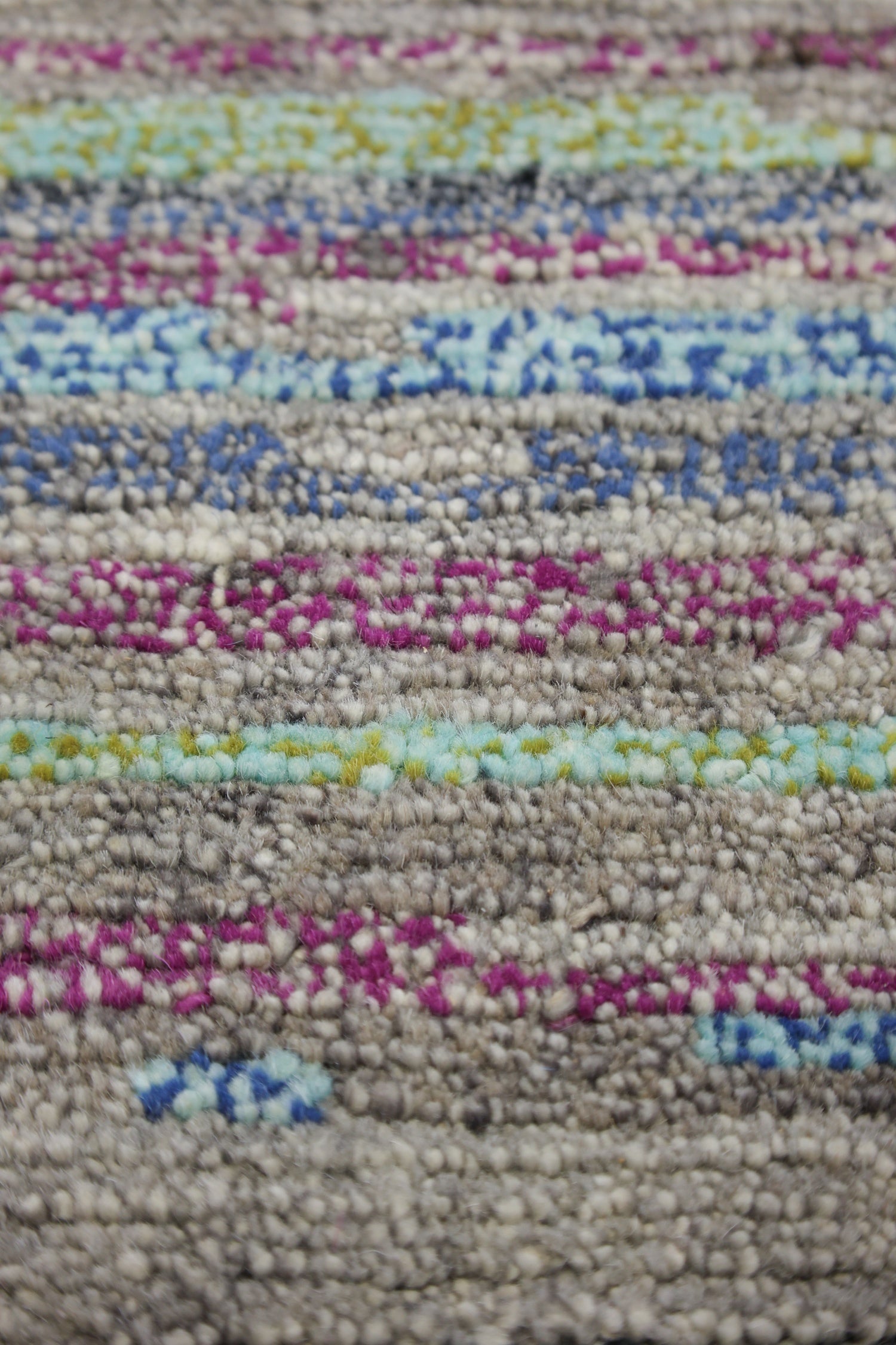 Close-up of handwoven rug detail; multicolored stripes in grey, pink, blue, and green.
