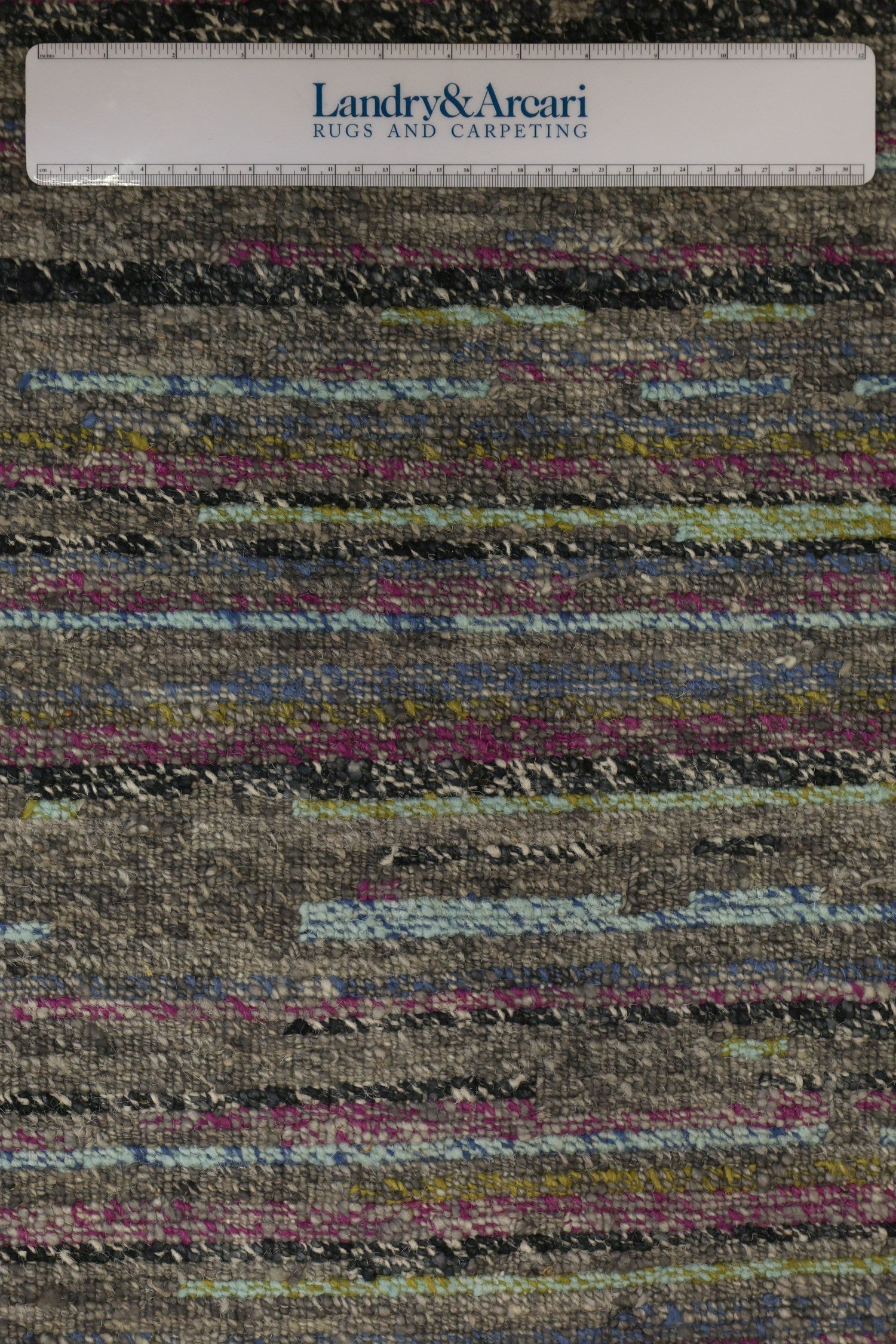 Handwoven rug detail, showcasing a textured weave with grey, pink, and blue hues.
