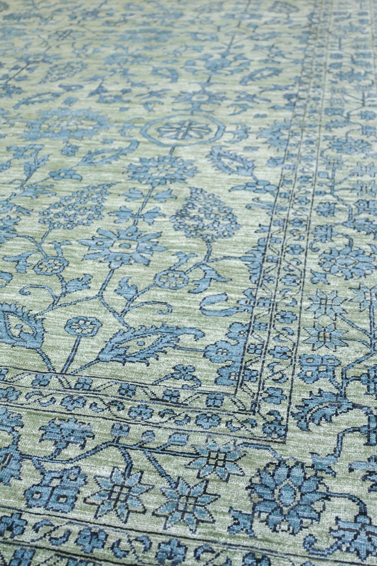 Handwoven rug detail, pale green with teal floral pattern.
