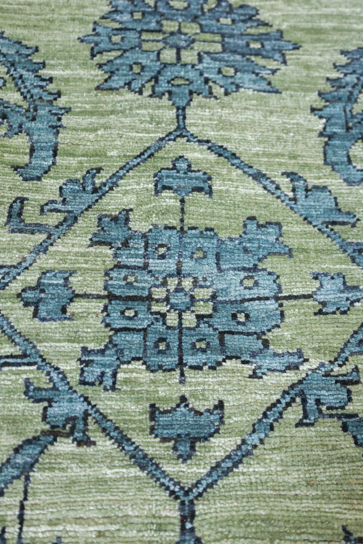 Close-up of a handwoven rug’s teal and sage green pattern.
