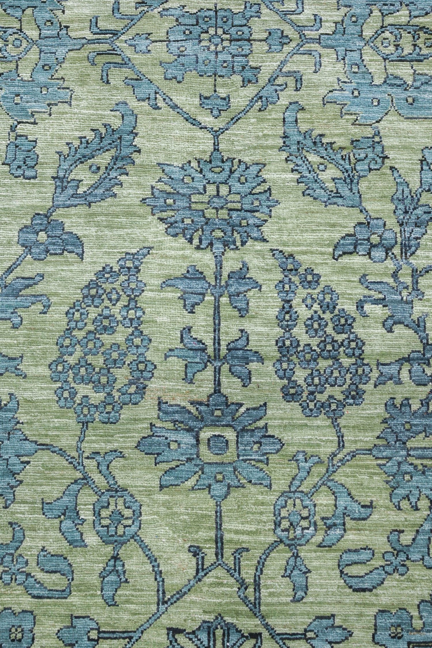 Handwoven rug detail: Pale green background with teal floral pattern.
