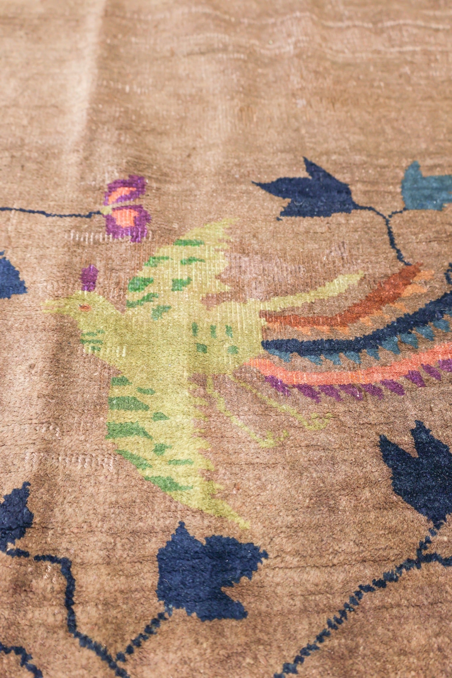 Close-up of an antique rug's handwoven detail, featuring a muted brown background and a colorful Art Deco bird design.
