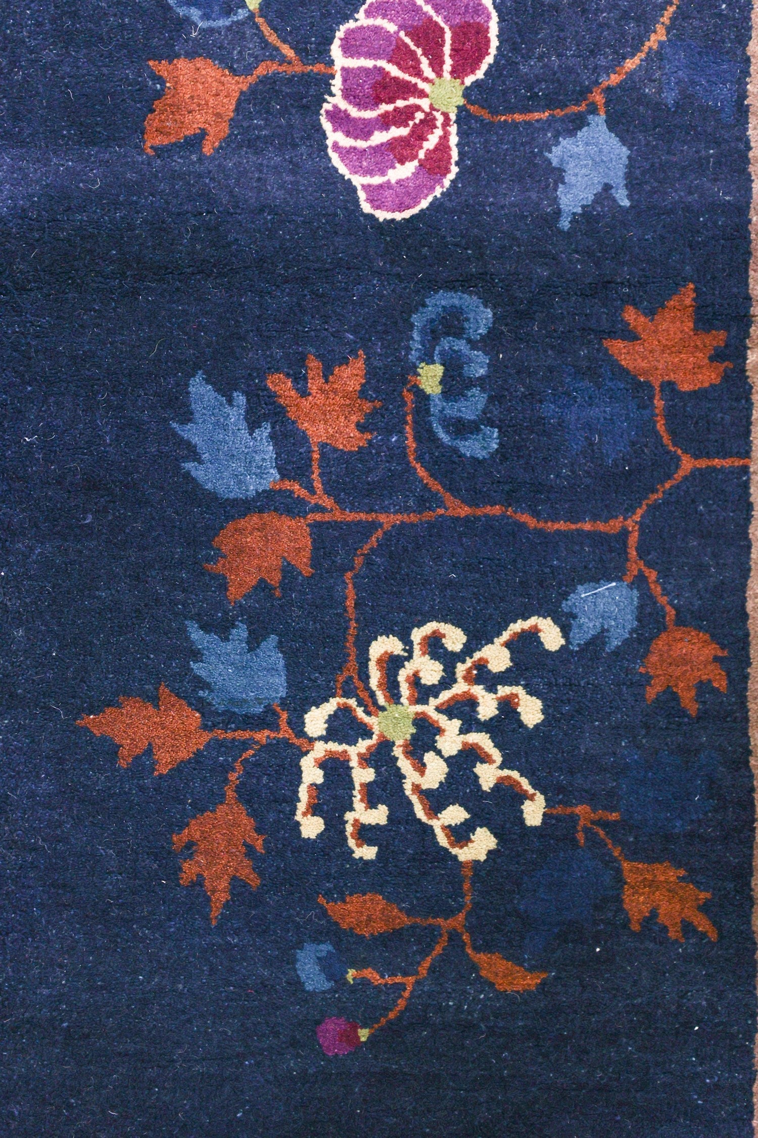 Detail of a navy blue antique rug with handwoven floral pattern in orange, purple, and cream.
