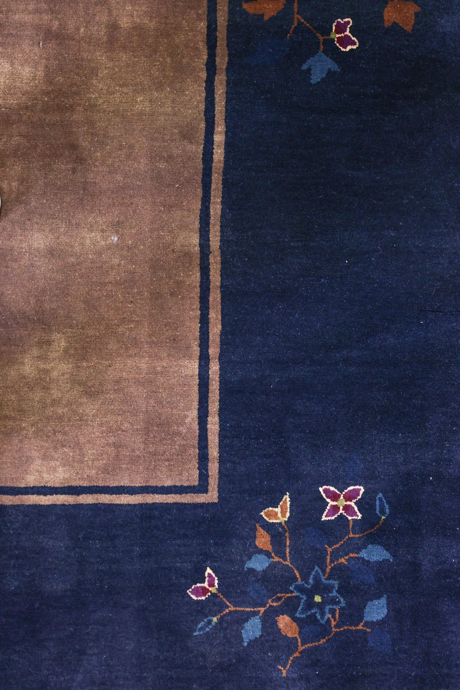 Detail of an antique Art Deco rug; navy blue field with a brown border and handwoven floral pattern.
