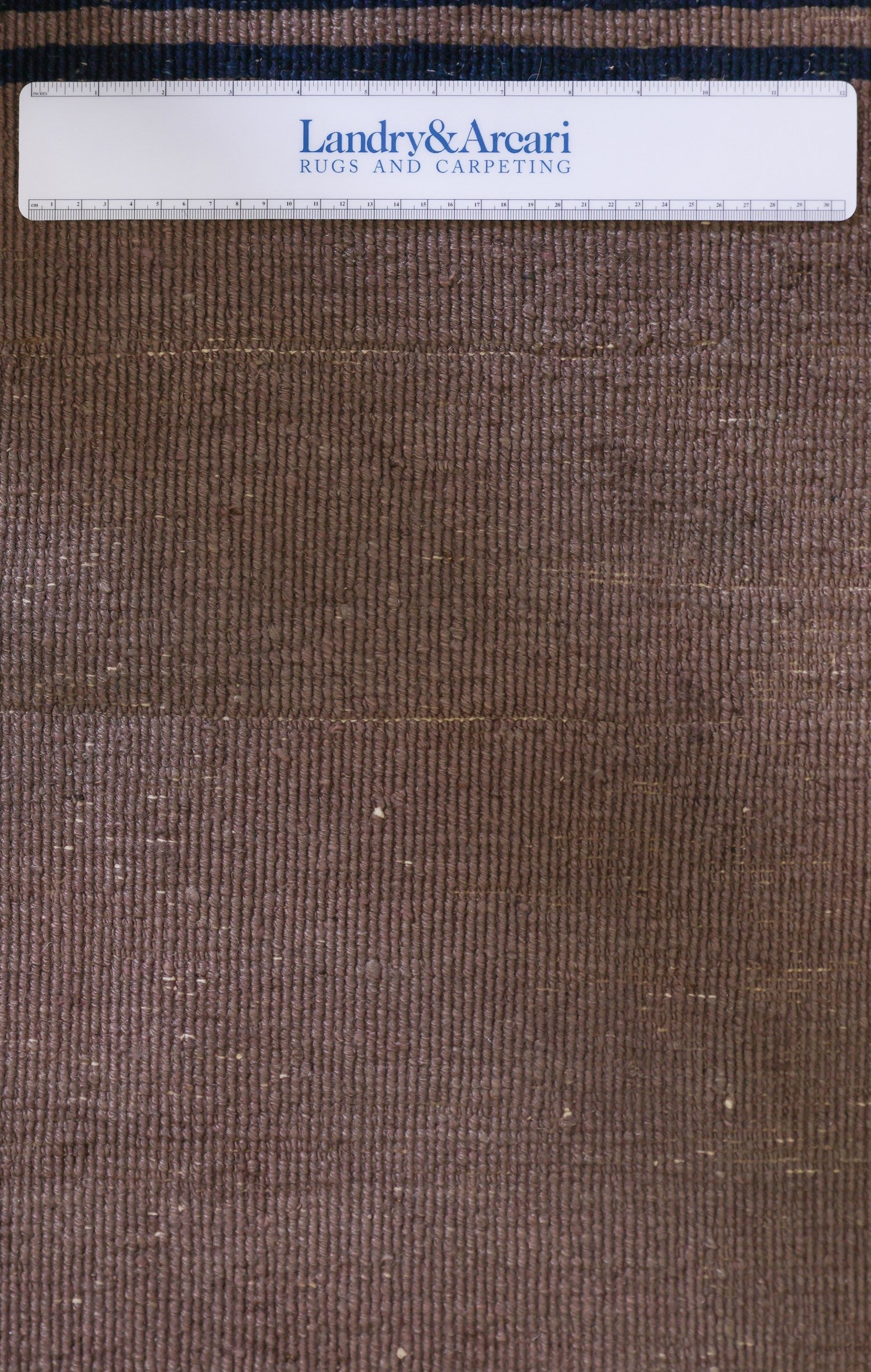 Close-up showing the detailed texture of a brown handwoven rug with subtle darker stripes.
