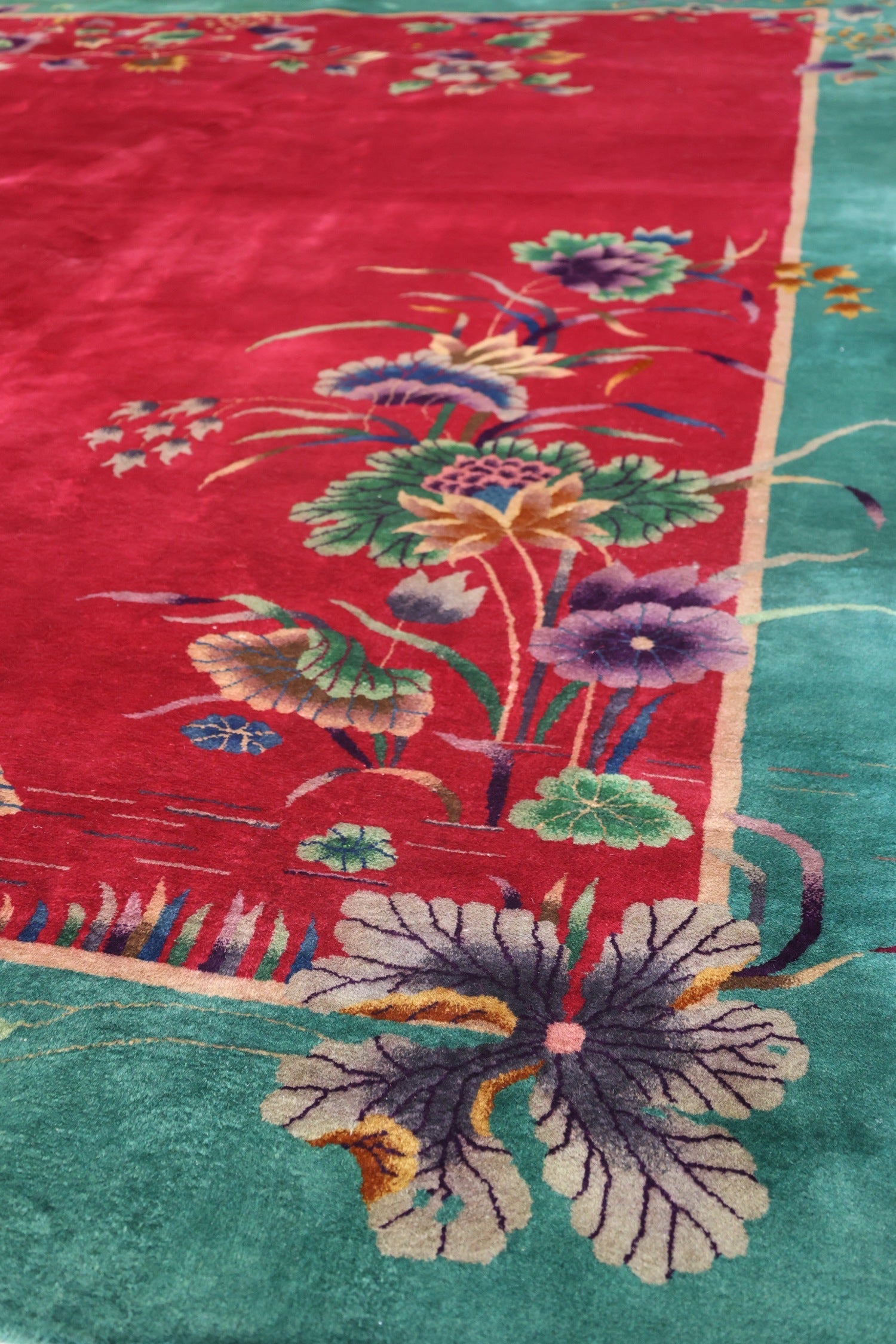 Detail of an antique handwoven rug, featuring a vibrant red and teal color palette with Art Deco floral patterns.
