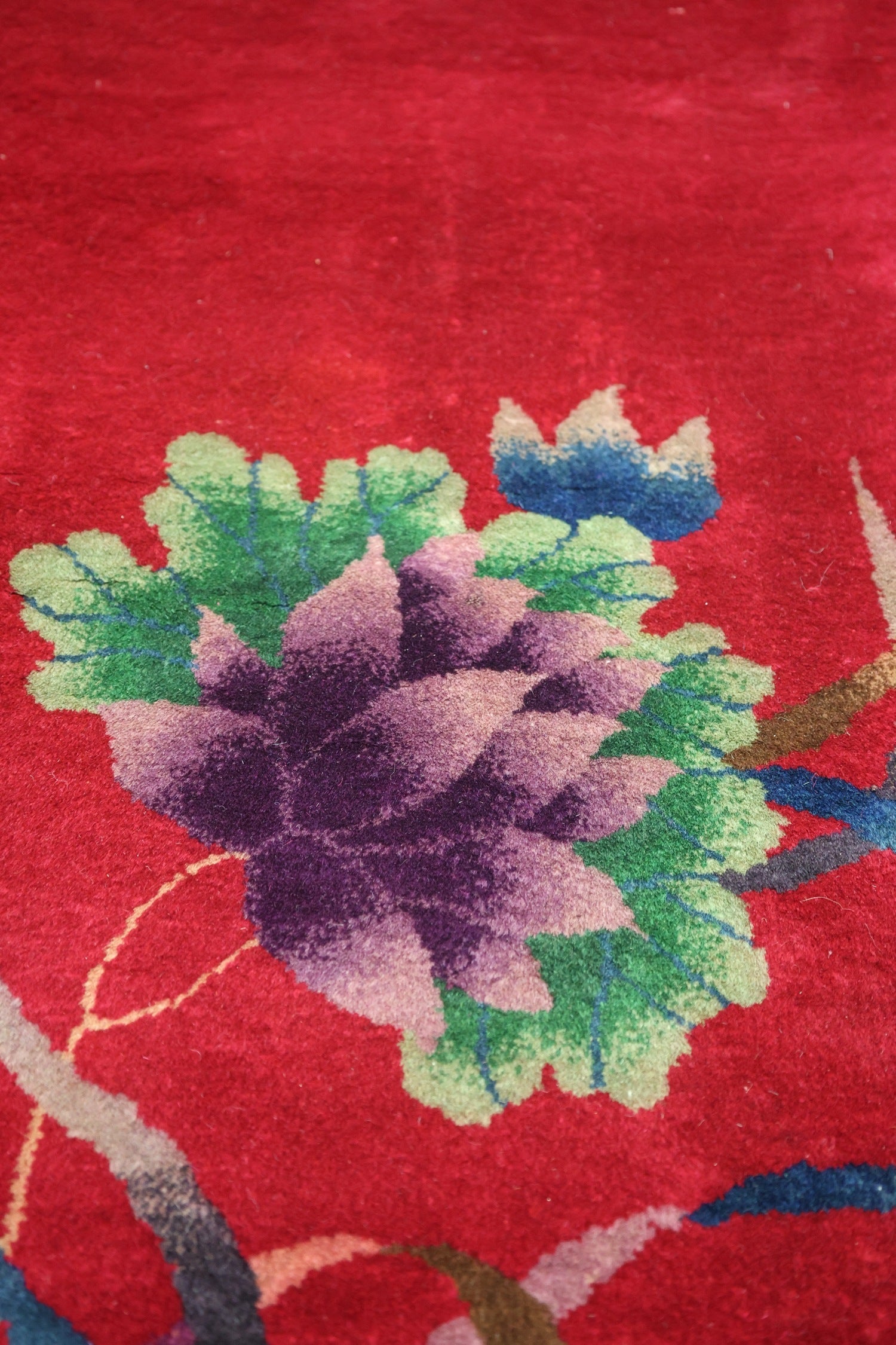 Close-up detail of a red Art Deco rug, showcasing a handwoven floral design with purple, green, and blue accents.
