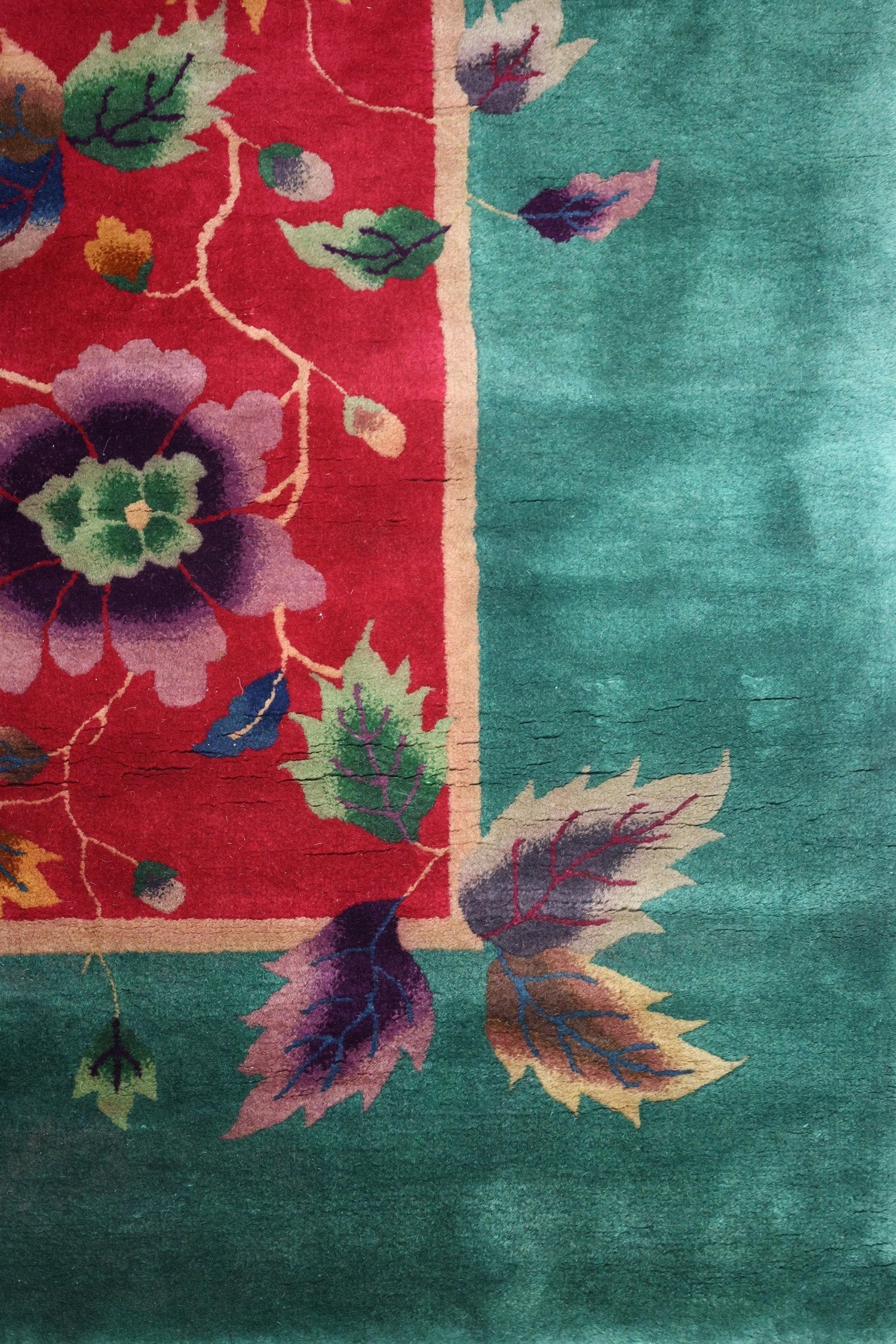 Close-up detail of a vintage Art Deco rug; handwoven with red and teal floral pattern.
