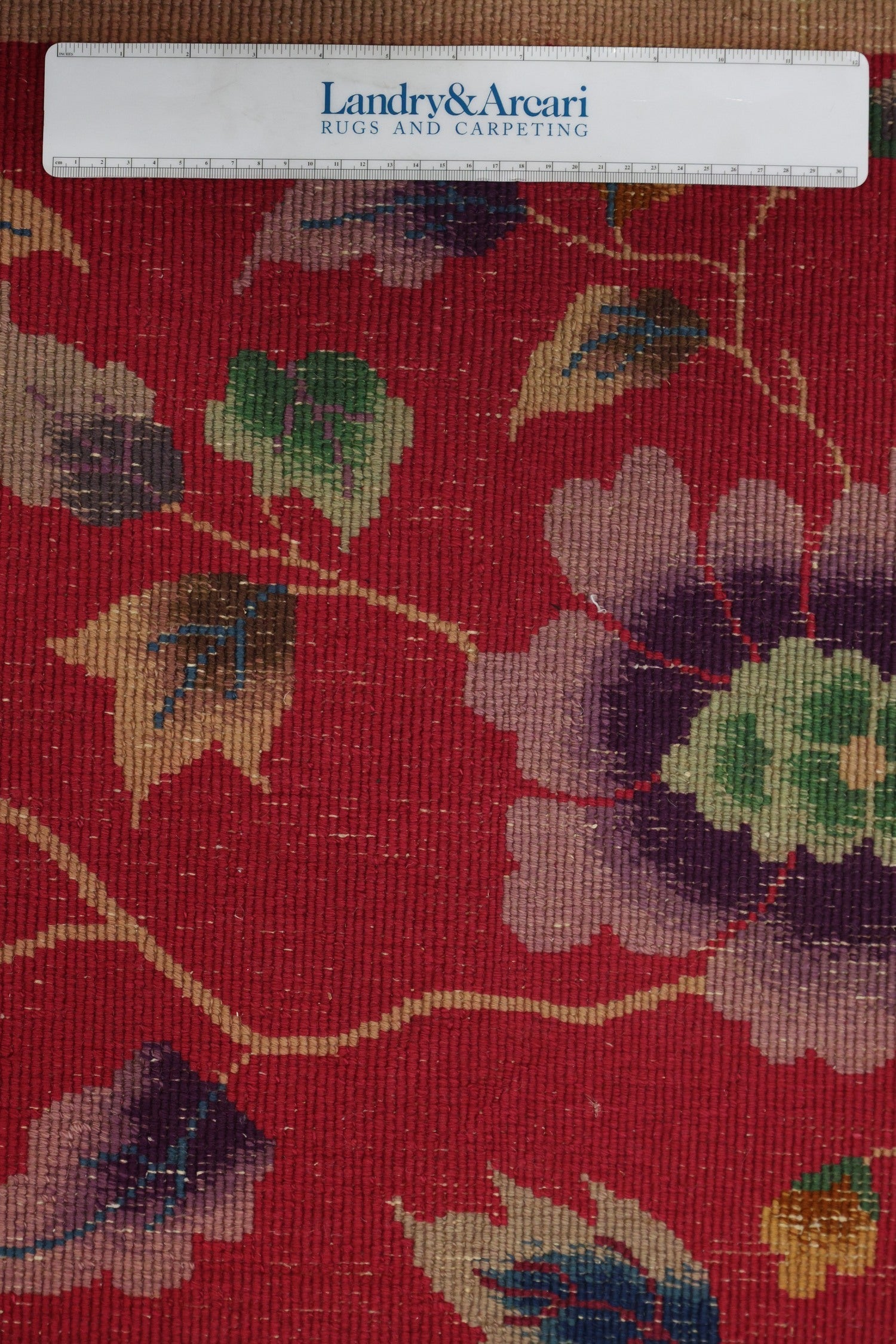 Close-up of antique rug detail, showcasing handwoven Art Deco floral pattern in red, purple, green, and beige tones.
