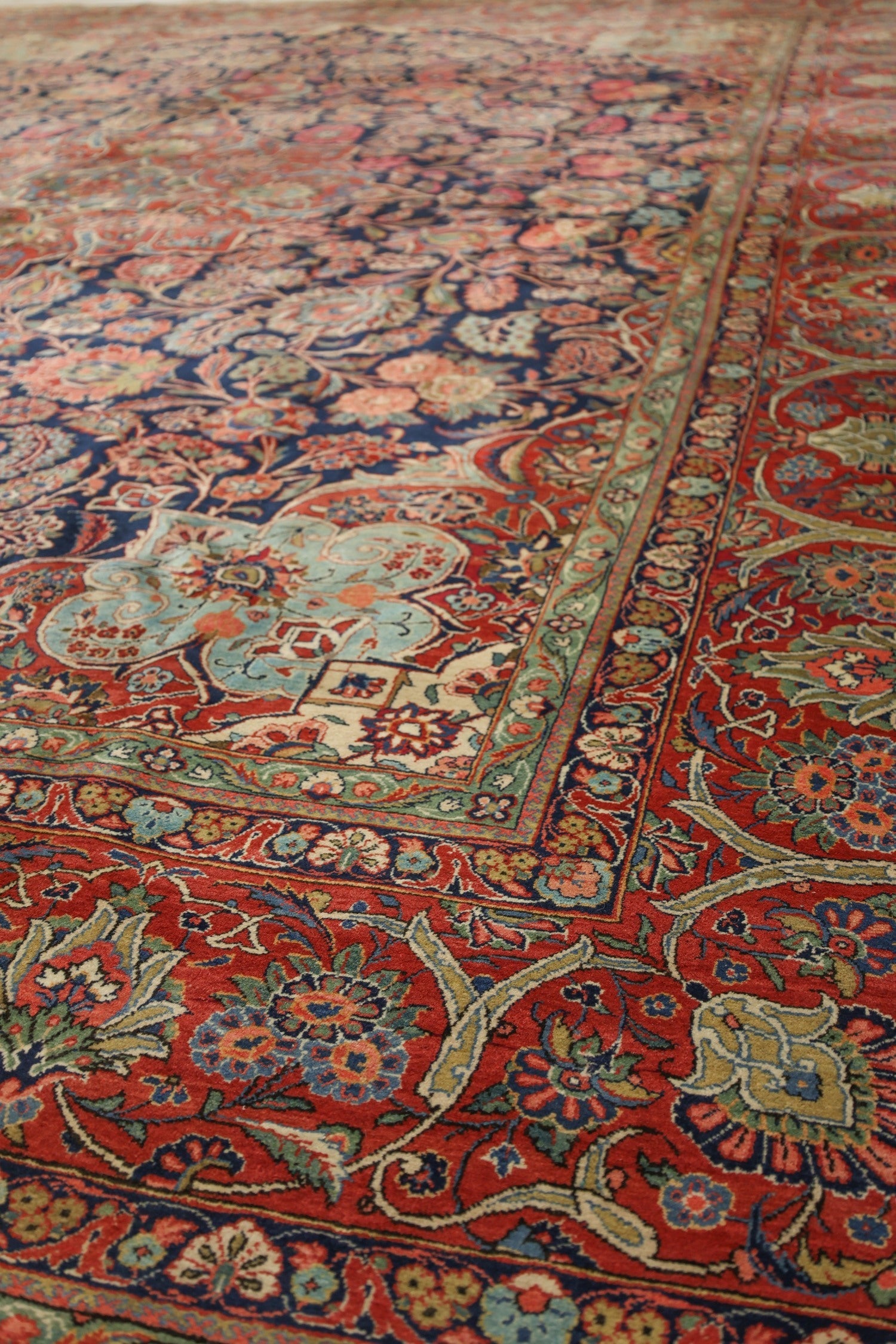 Detail of antique handwoven rug, showcasing intricate floral patterns in red, blue, and green hues.
