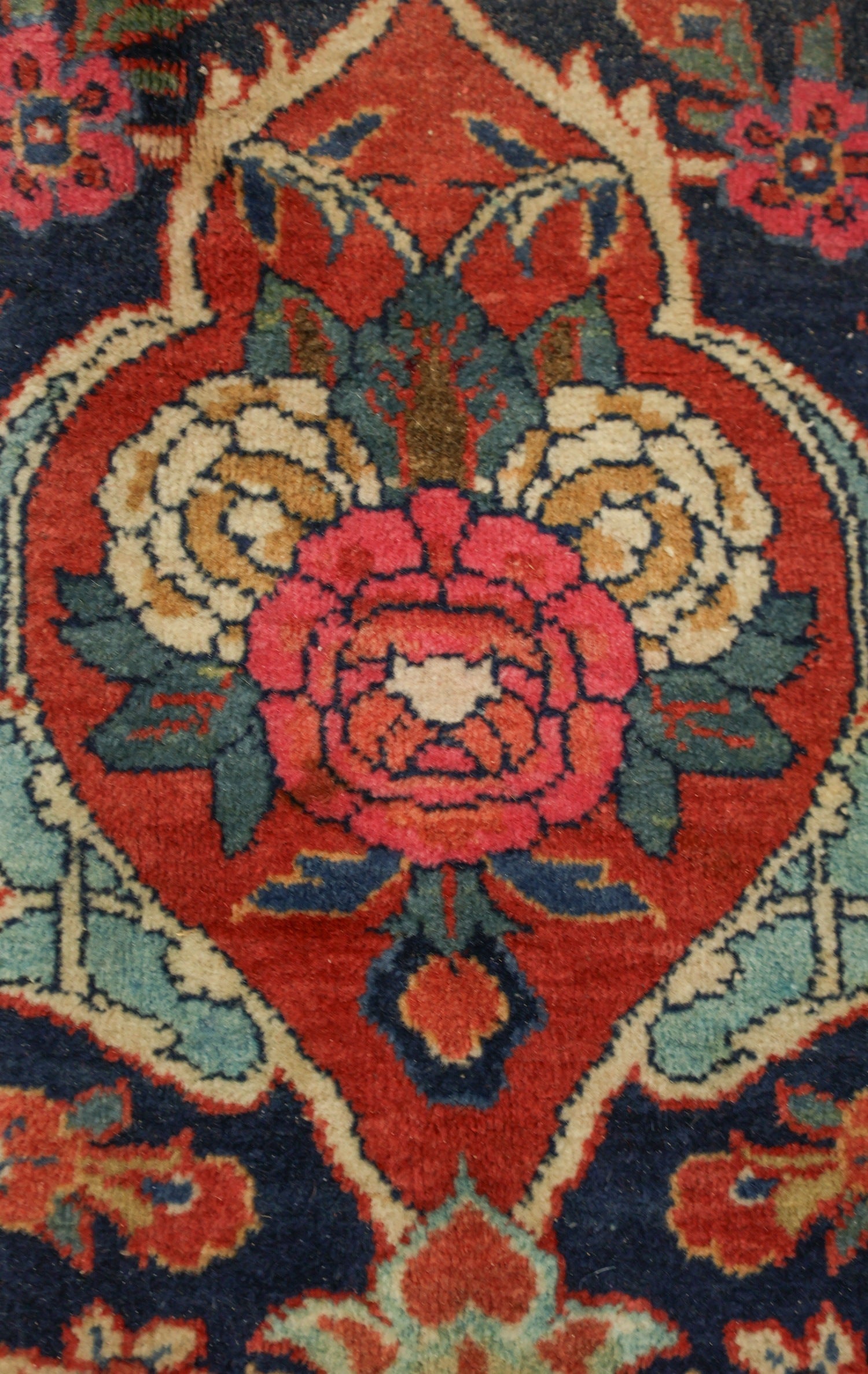 Close-up detail of antique rug's floral pattern, rich red and blue tones, handwoven texture.
