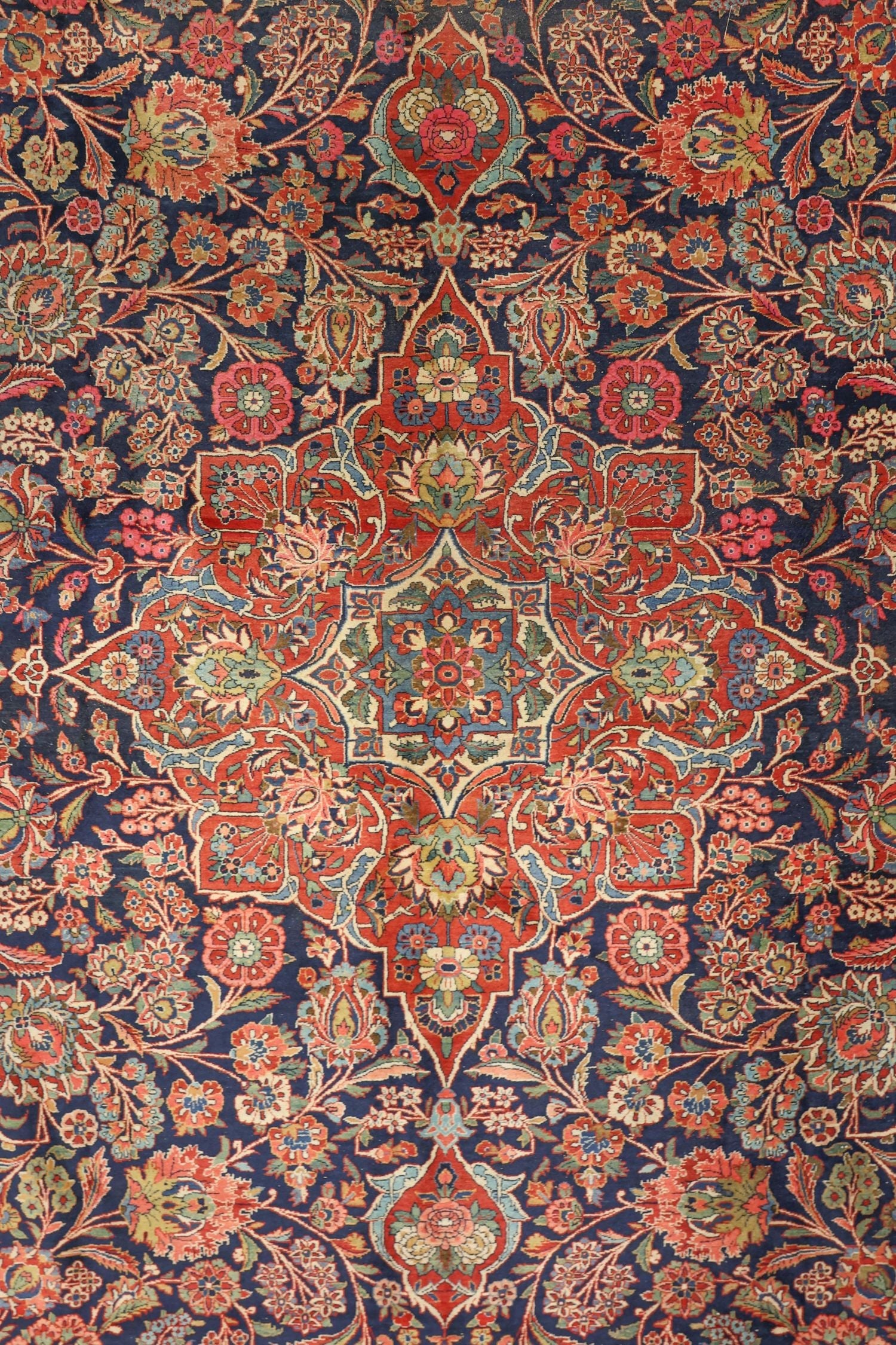 Intricate floral detail on a traditional antique rug, rich navy base with red and cream accents.
