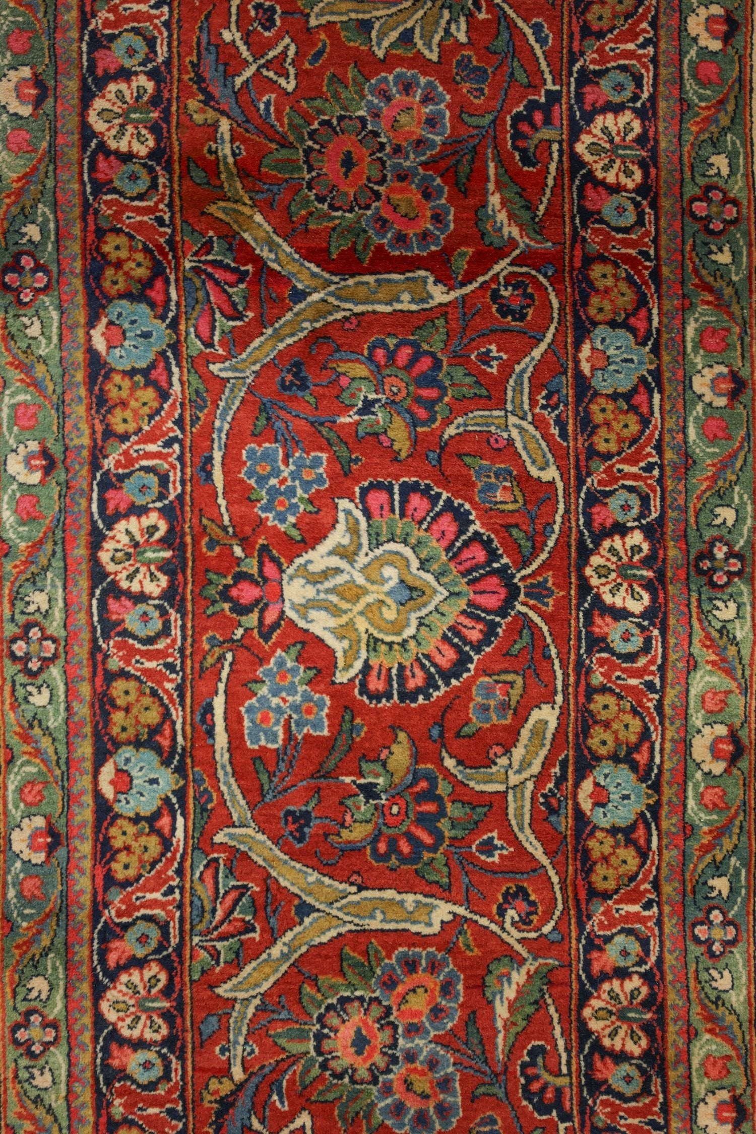 Close-up of antique rug detail; vibrant floral pattern in red, blue, and green hues.
