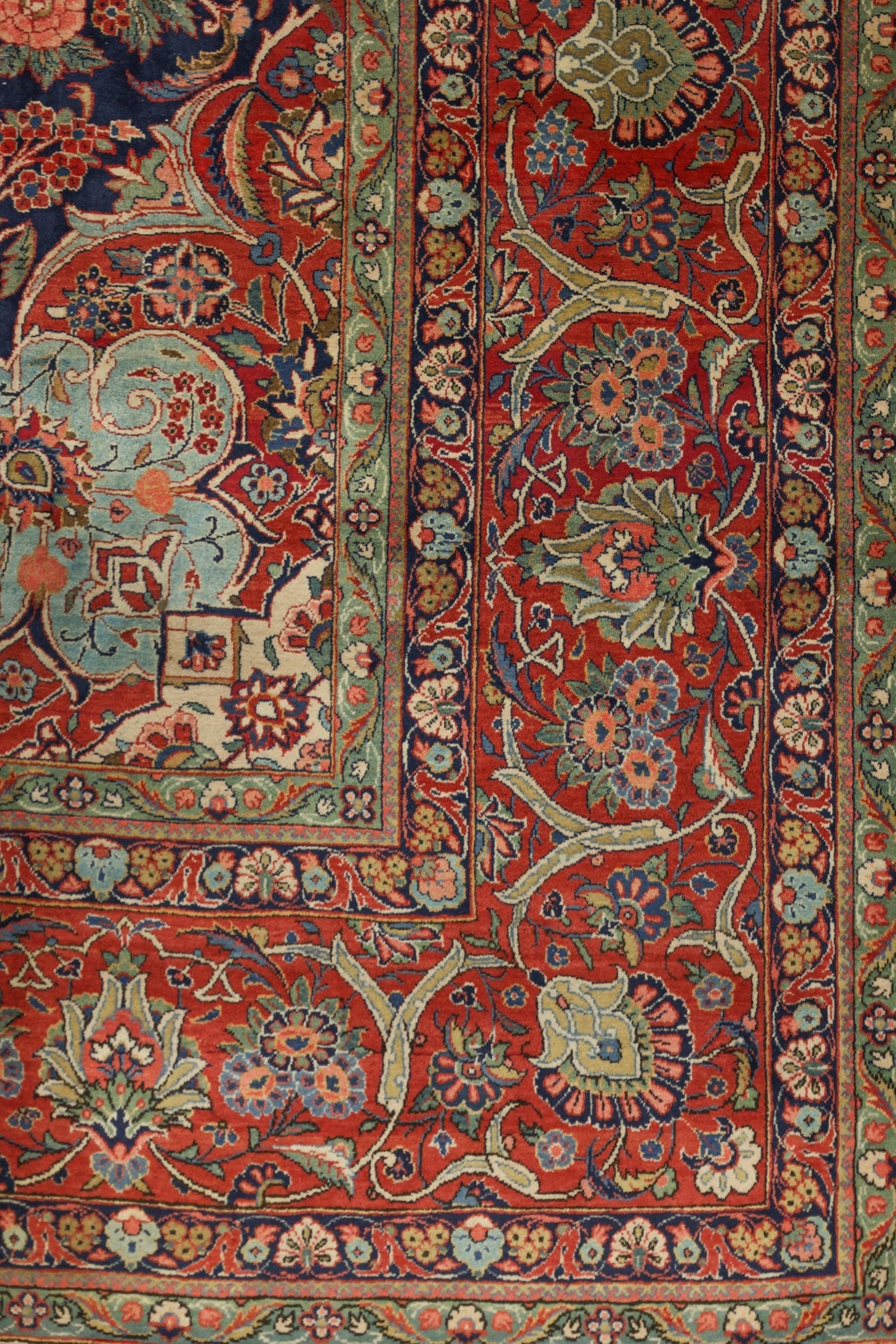 Detail of antique handwoven rug, showcasing intricate floral pattern in red, blue, and green.
