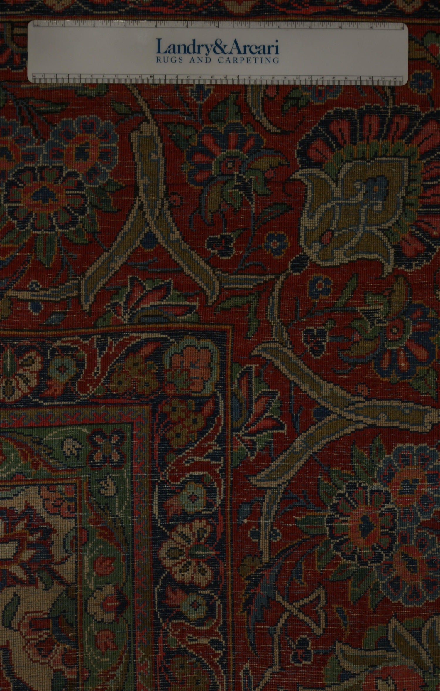 Detailed close-up of antique rug's intricate floral pattern, showcasing rich reds and blues.
