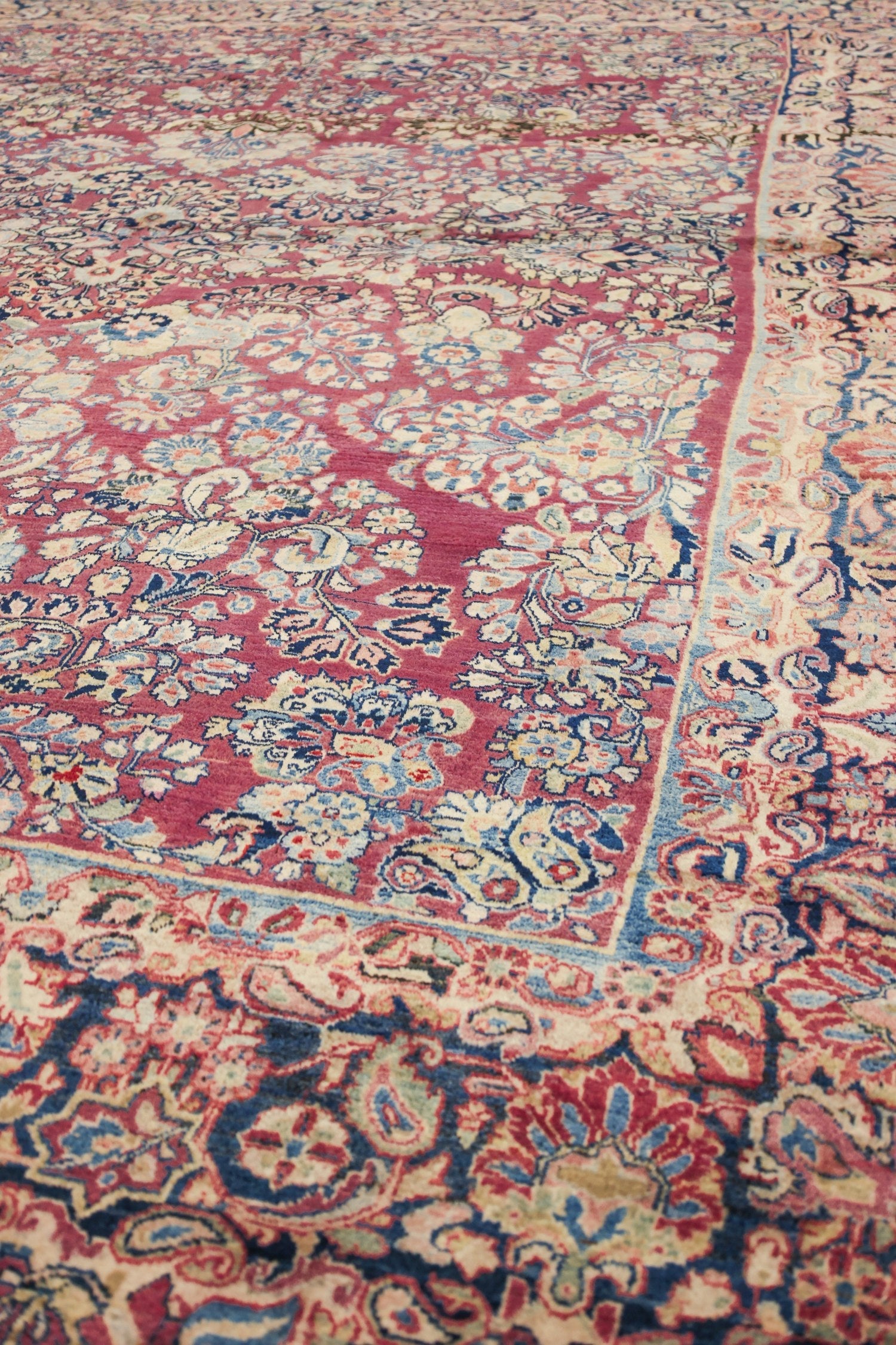 Close-up of antique rug's detailed floral pattern in red, blue, and beige.
