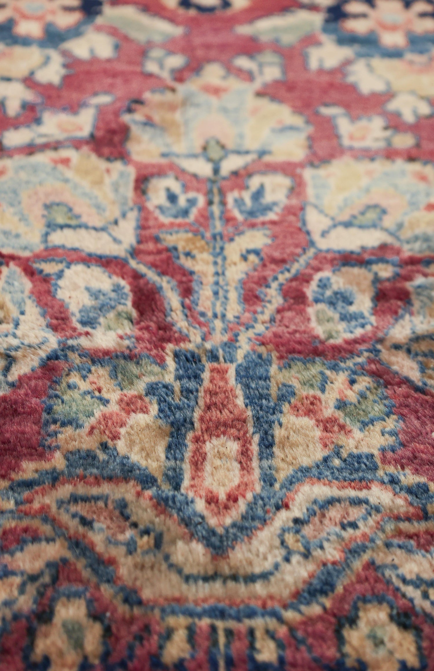 Close-up of antique rug's detailed handwoven pattern in muted reds, blues, and beige.
