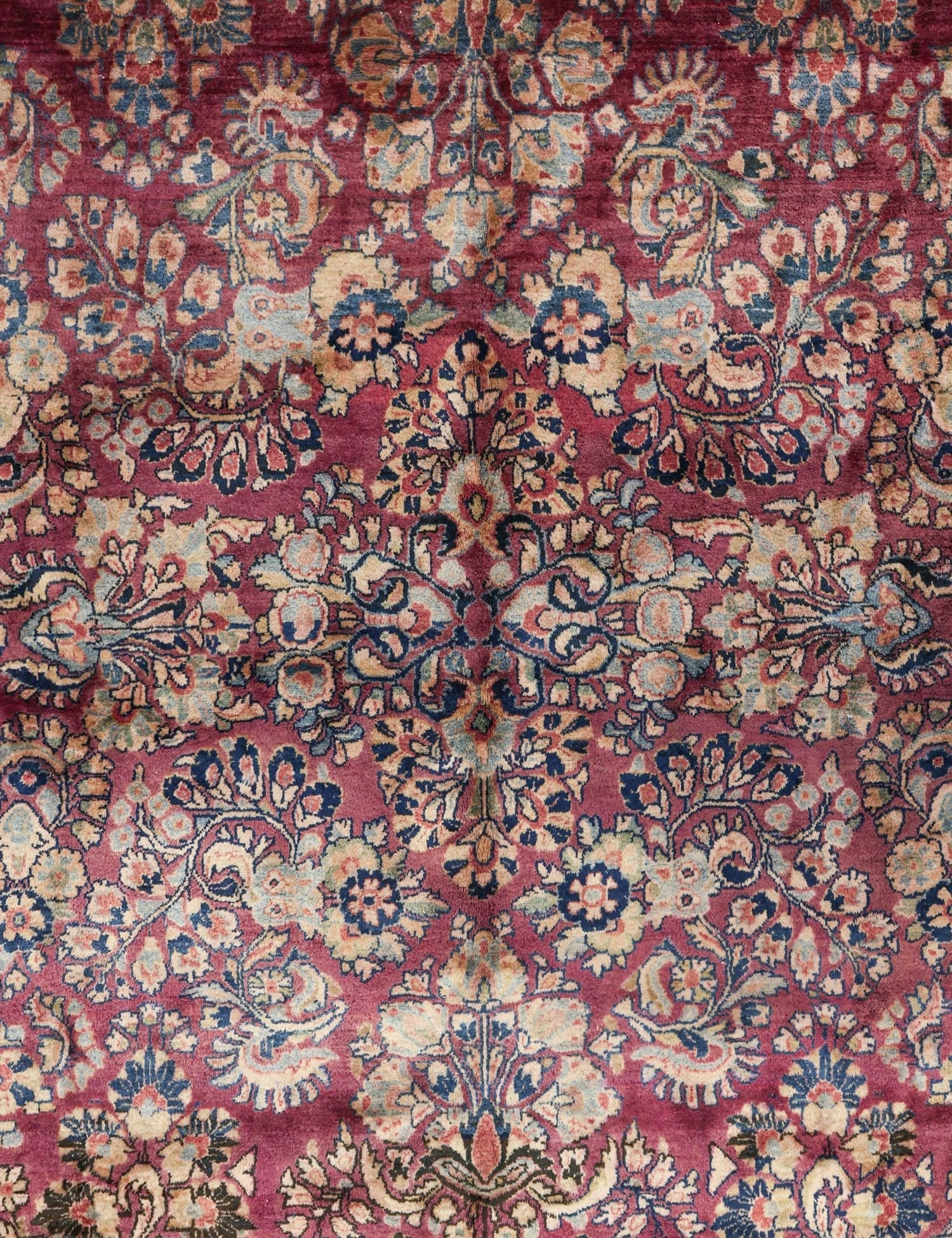 Detailed close-up of a vintage rug's rich, floral pattern in muted reds and blues.
