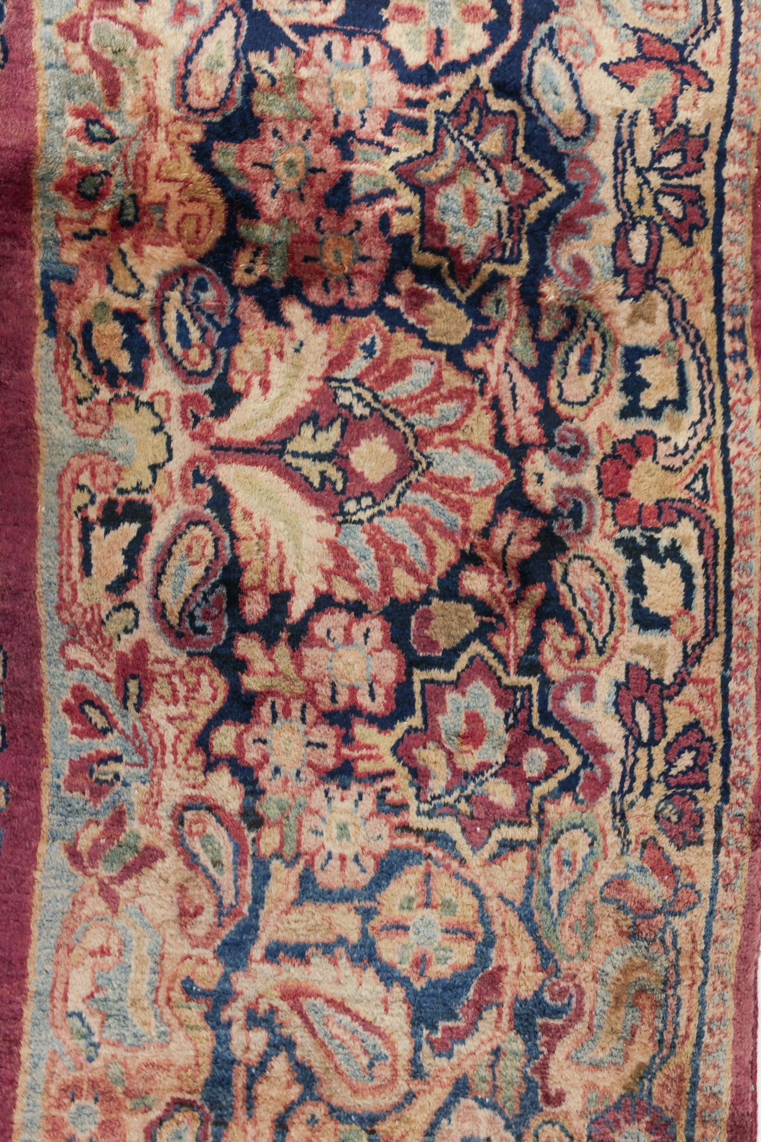 Close-up of antique rug's handwoven floral pattern in red, beige, and navy.
