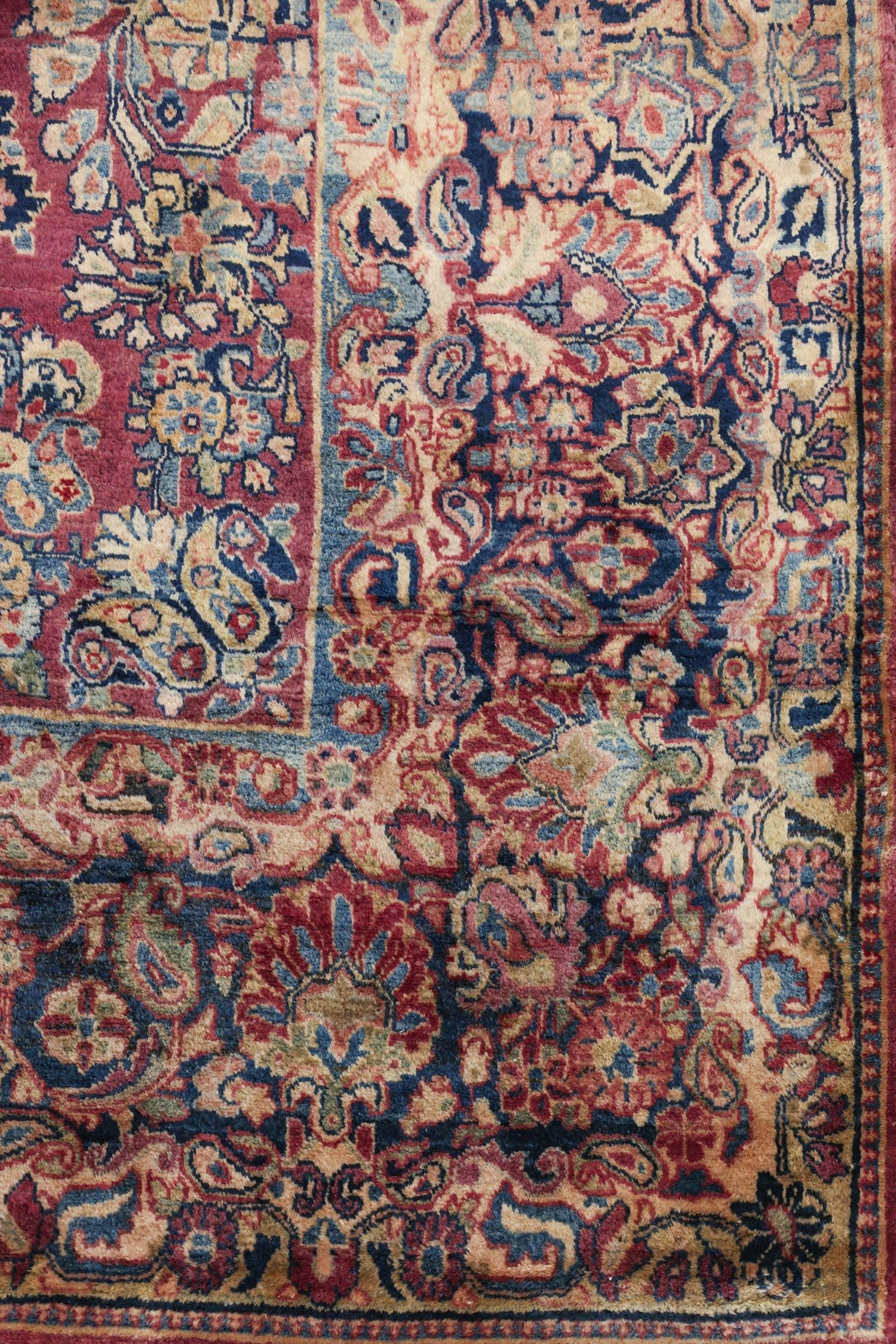 Antique handwoven rug detail, showcasing a rich tapestry of reds, blues, and creams in a traditional floral pattern.
