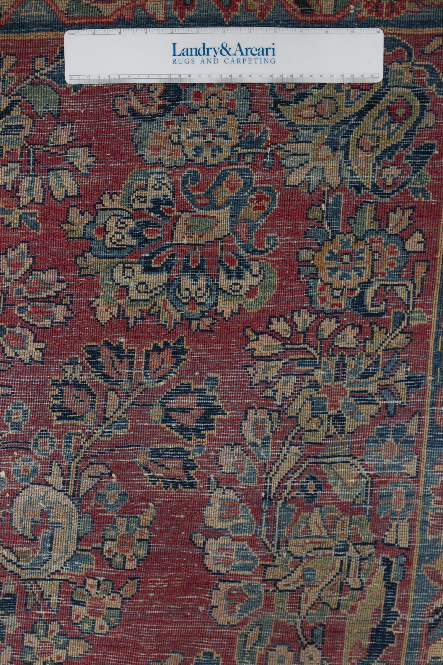 Detailed close-up of an antique rug's intricate, handwoven floral pattern in muted reds and blues.
