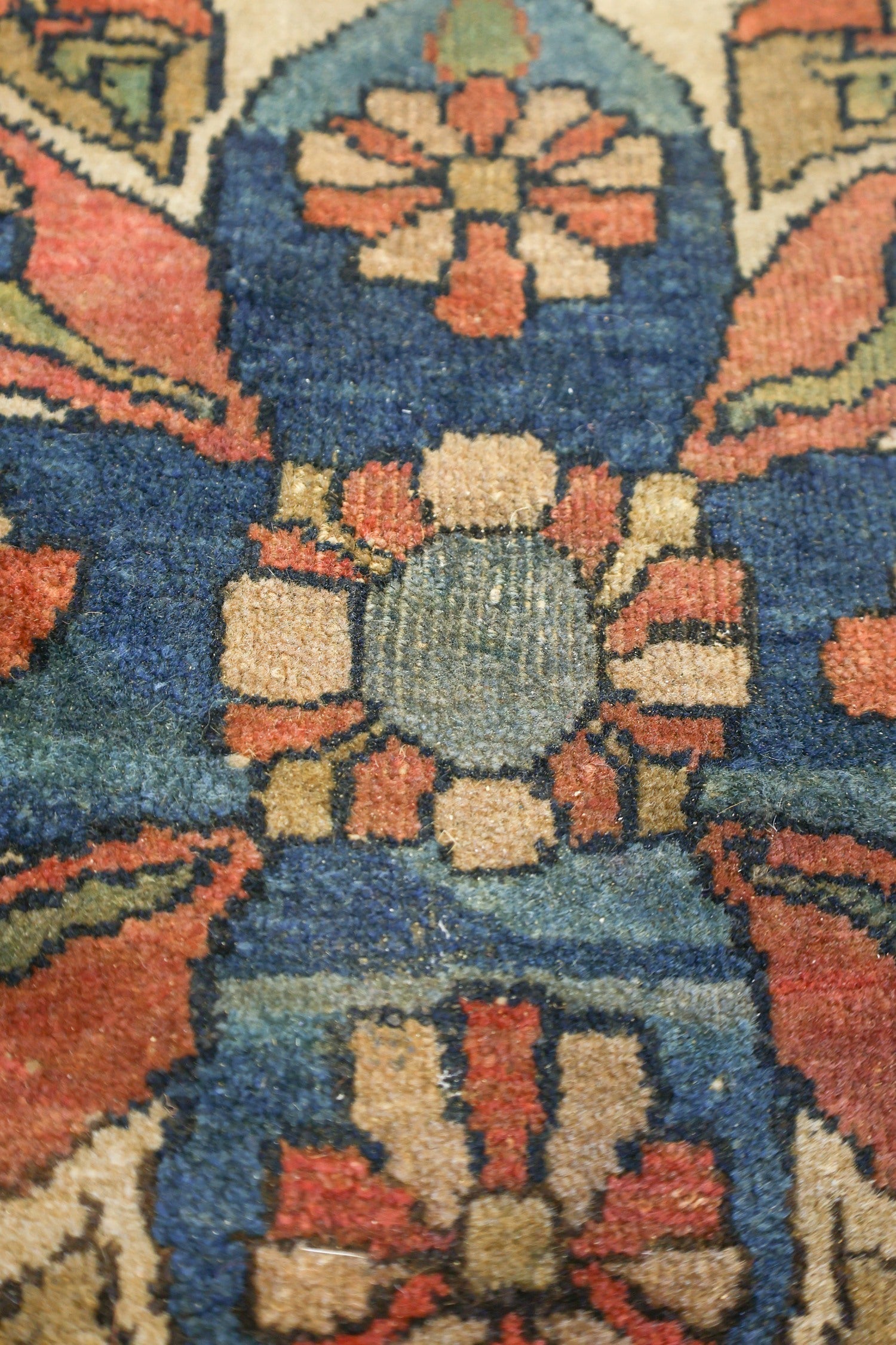 Close-up detail of a traditional handwoven rug, showcasing intricate floral patterns in deep blues, reds, and beige tones.
