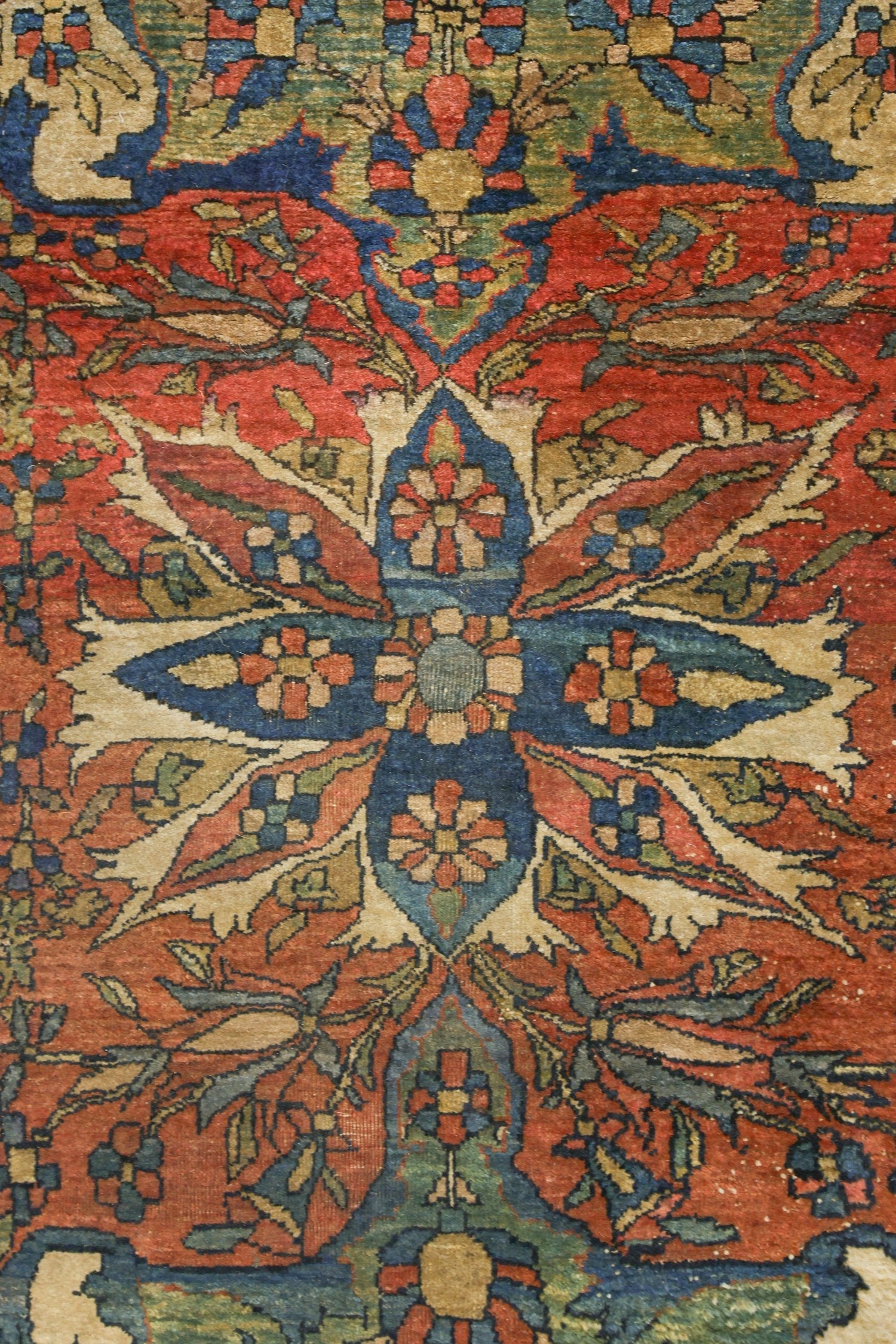 Detail of antique rug's handwoven floral pattern in red, blue, and beige.
