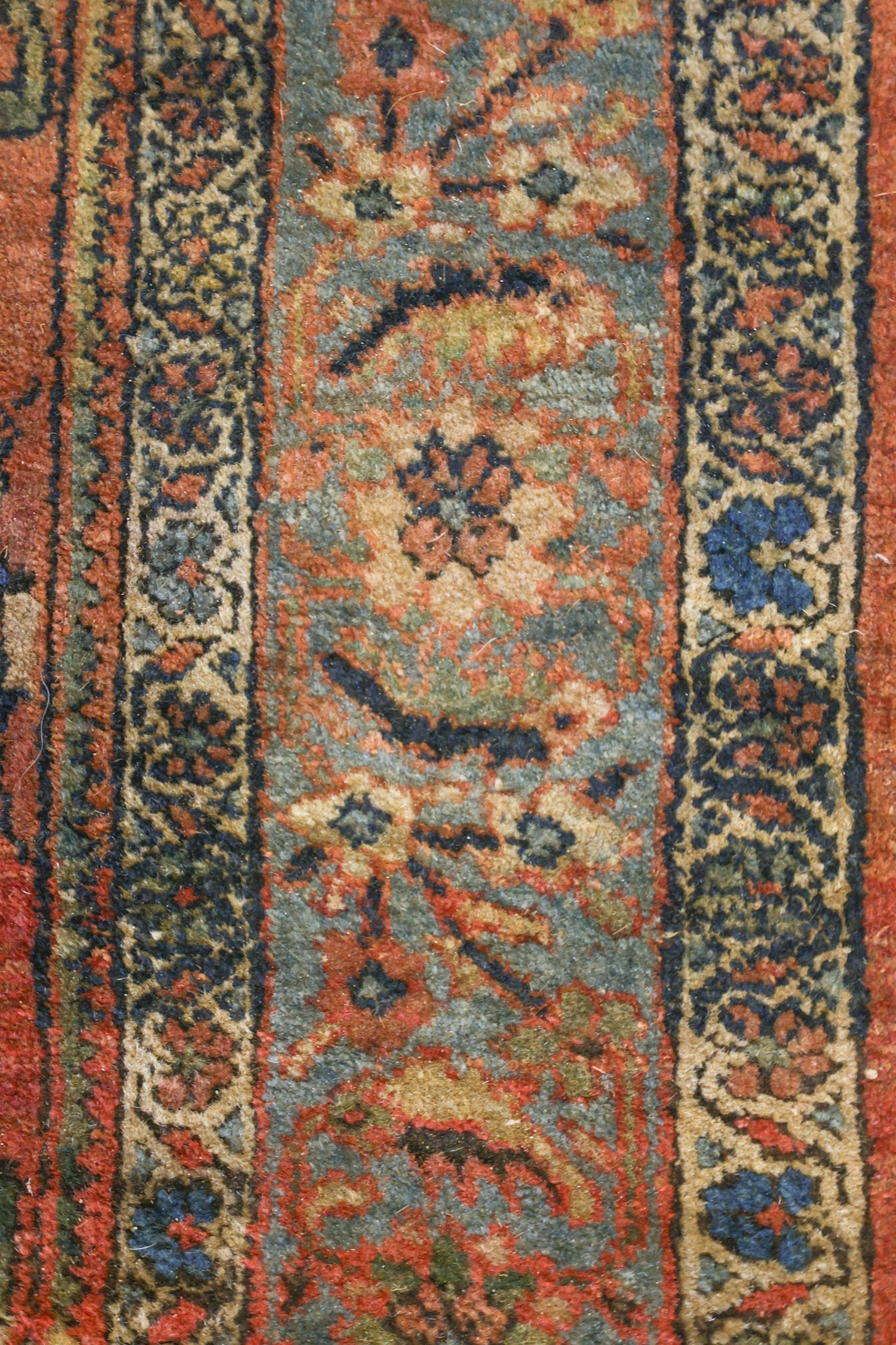 Close-up detail of a vintage rug's handwoven floral pattern in muted reds, blues, and beige.
