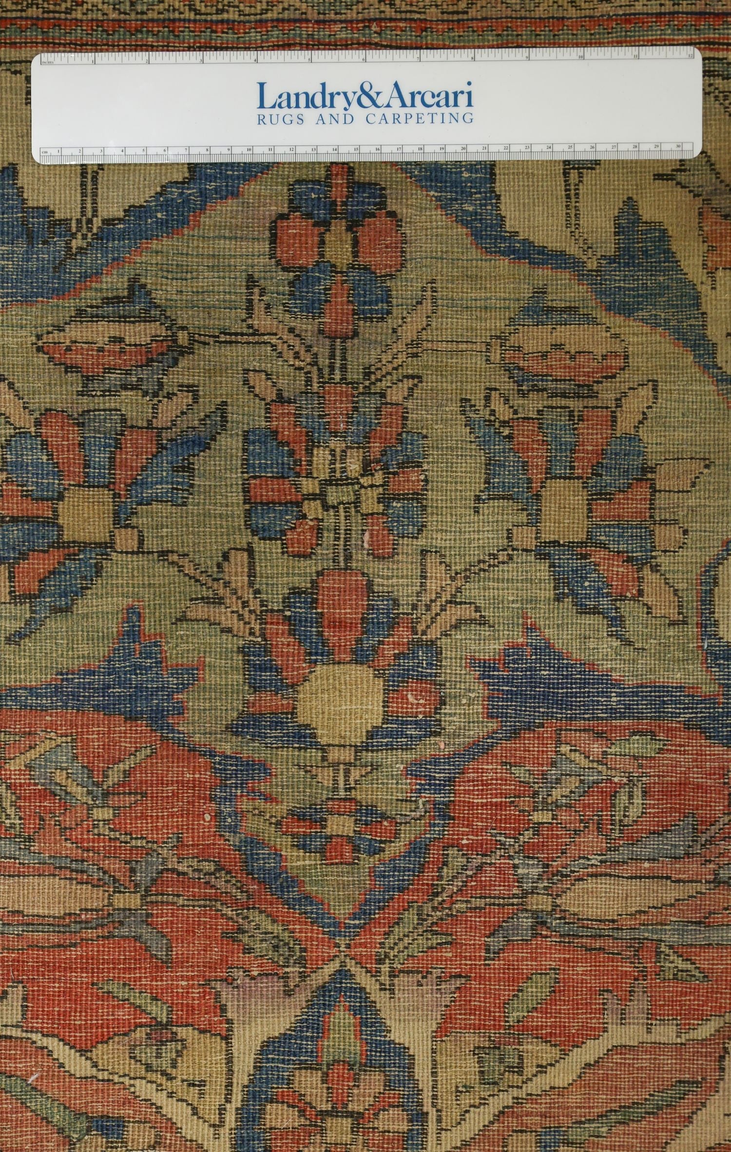 Close-up detail of antique rug's handwoven floral pattern in red, blue, and beige.
