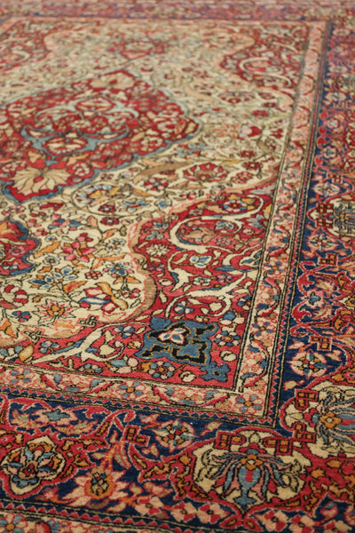 Close-up of antique Isfahan rug's intricate floral pattern in red, blue, and beige.
