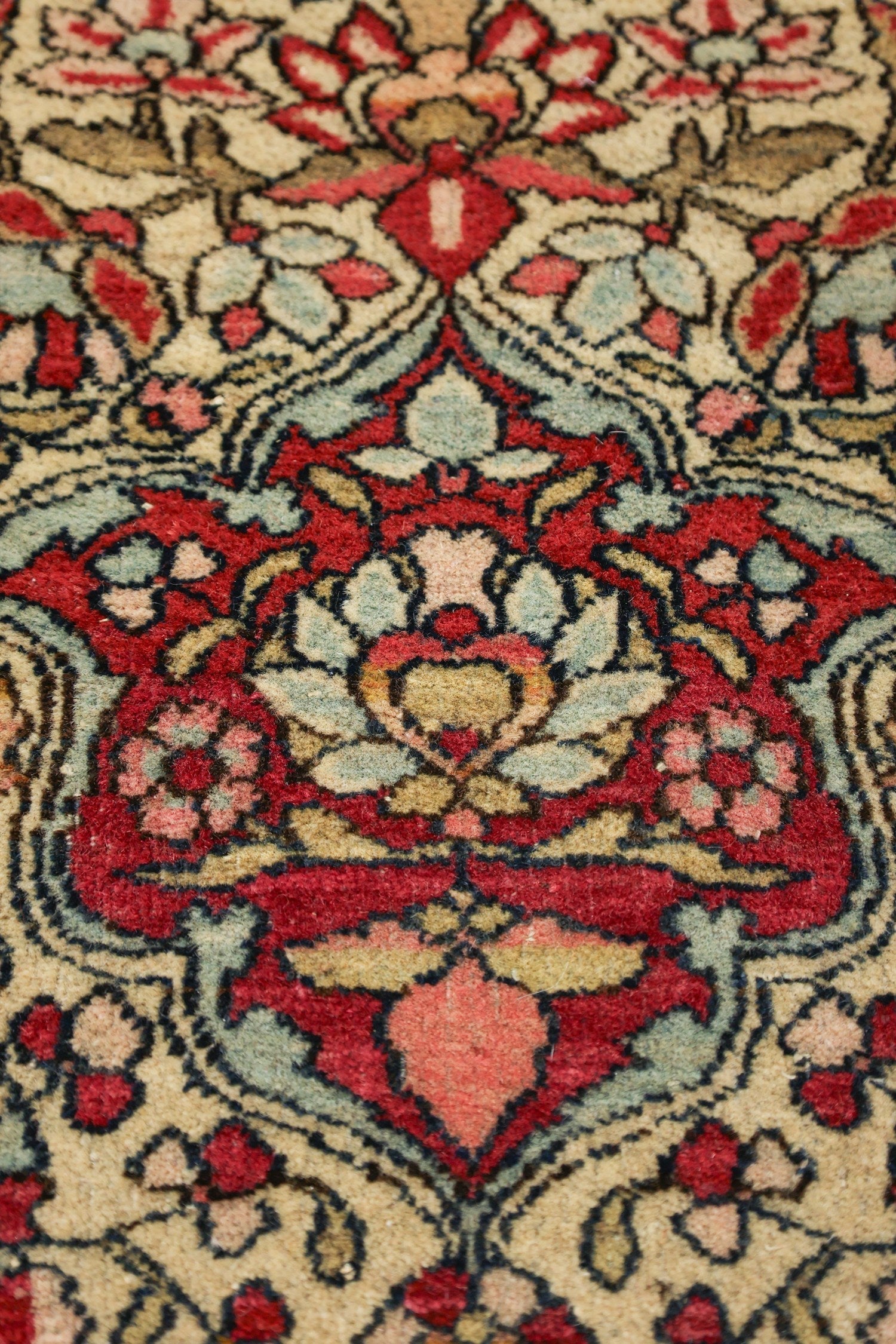 Close-up of antique Isfahan rug detail, showcasing intricate floral pattern in red, beige, and teal.
