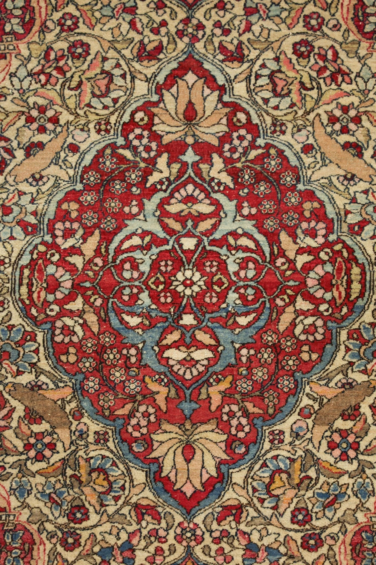 Detailed close-up of an antique Isfahan rug's intricate floral pattern in red, blue, and beige.
