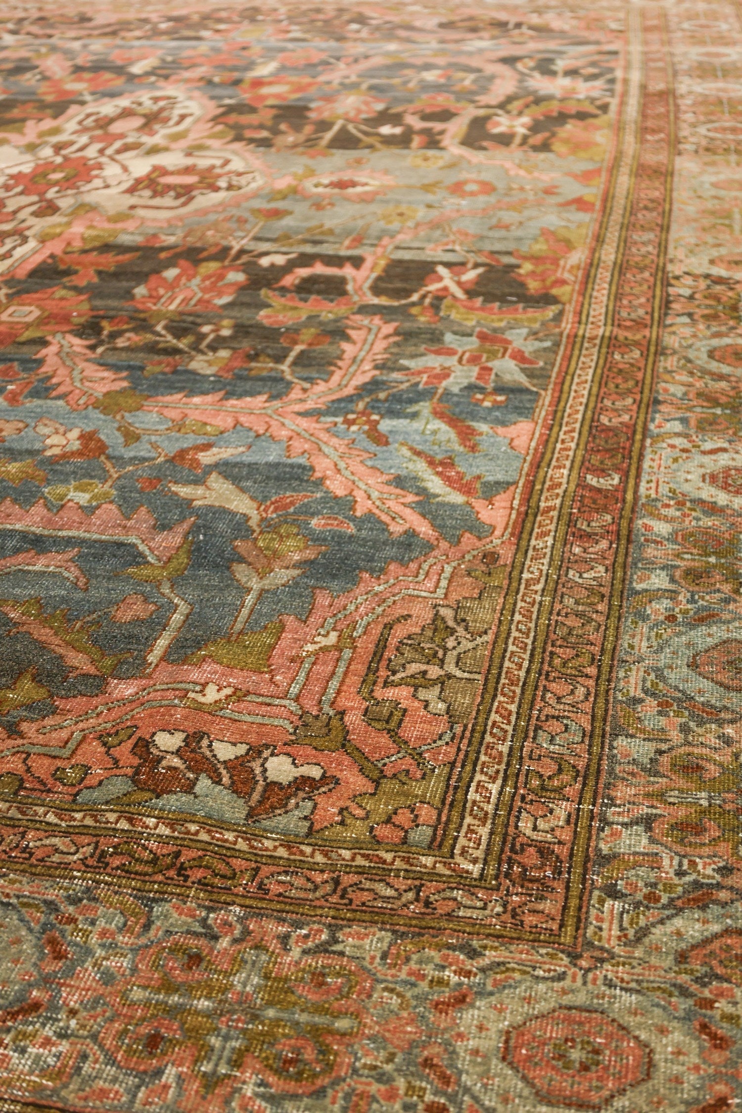 Close-up of antique rug's detailed handwoven floral pattern, muted pink and teal tones.
