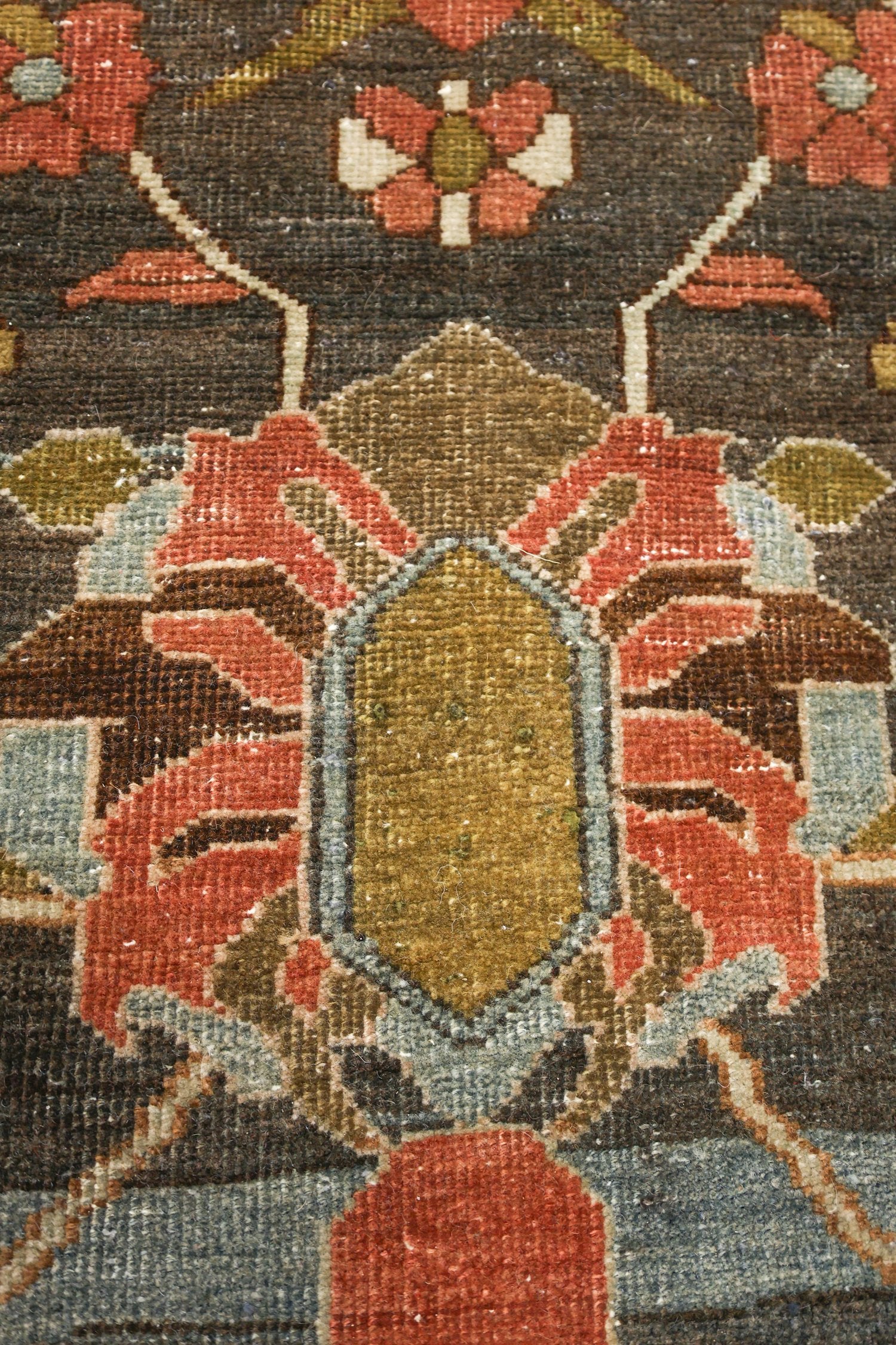 Close-up detail of a traditional handwoven rug, showcasing its intricate floral pattern in muted reds, browns, and greens.
