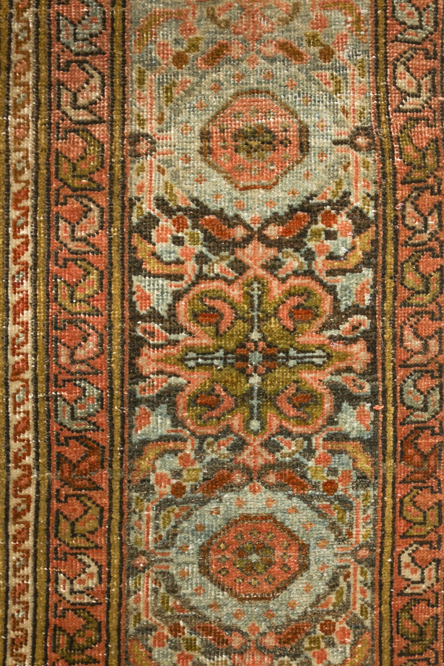 Close-up of antique rug detail, showcasing intricate handwoven floral pattern in muted reds, greens, and blues.
