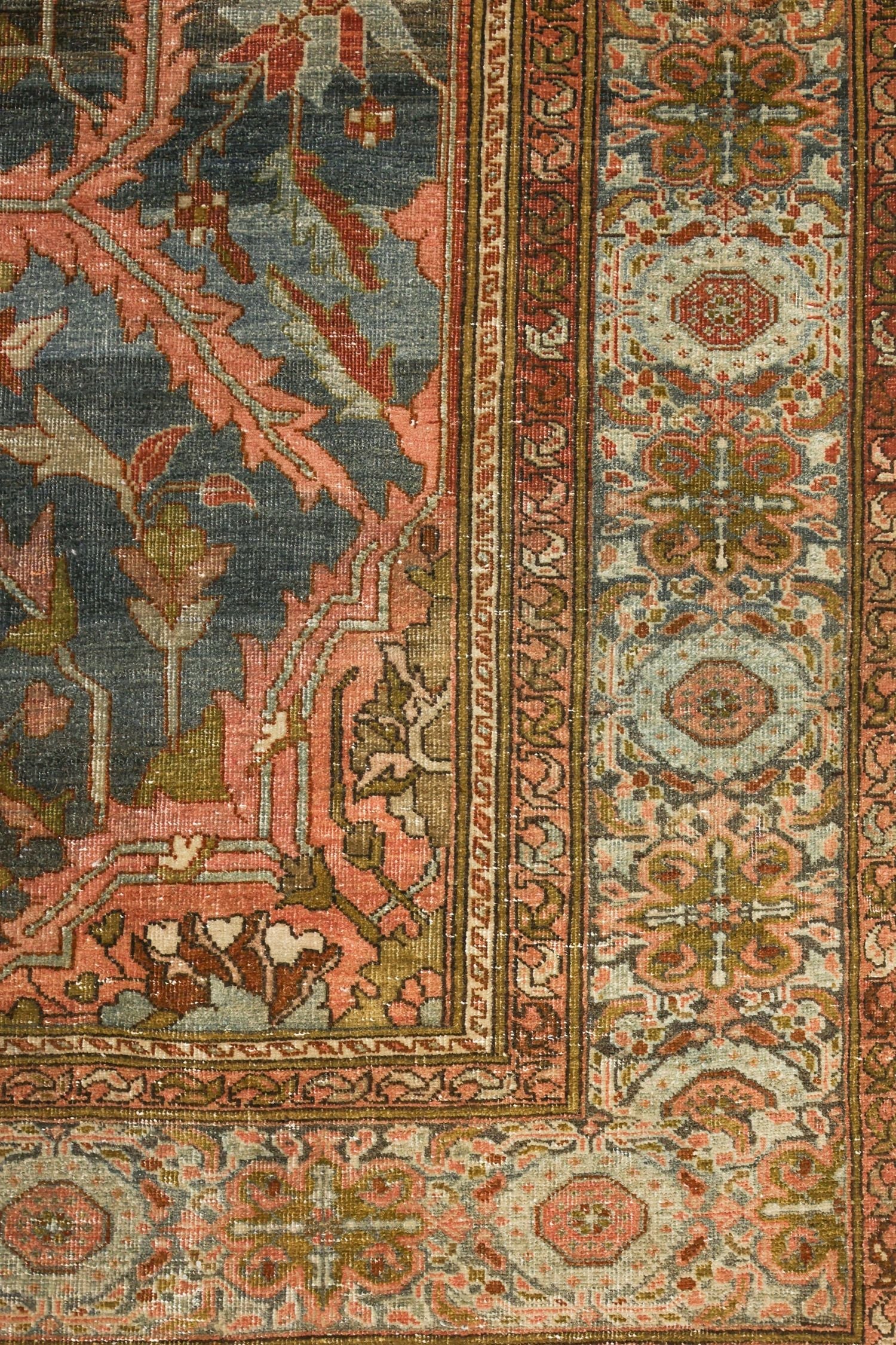 Detail of antique Sarouk rug, showcasing handwoven floral patterns in muted pinks, greens, and blues.
