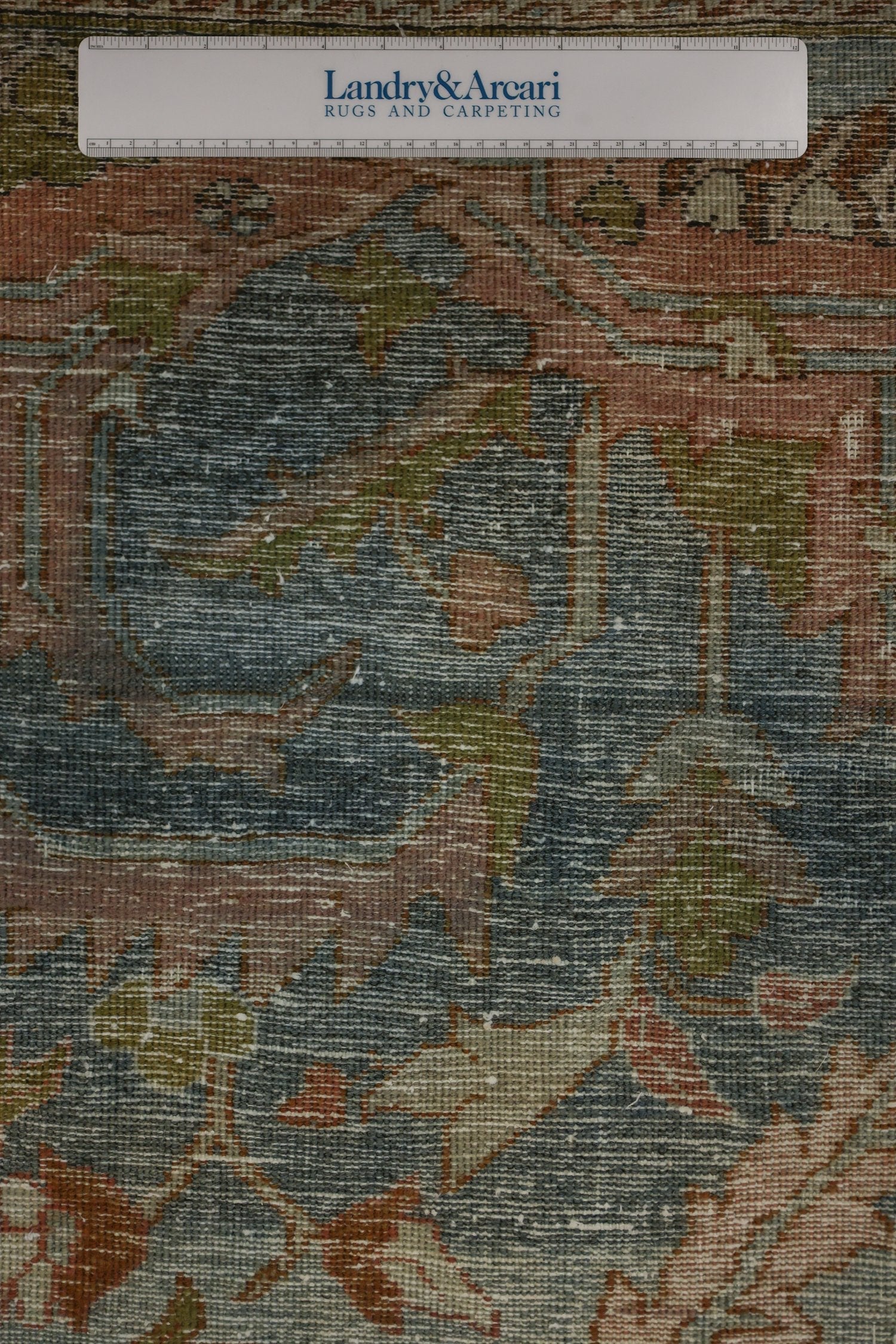 Close-up detail of antique rug's handwoven texture, showcasing muted blues, pinks, and greens.
