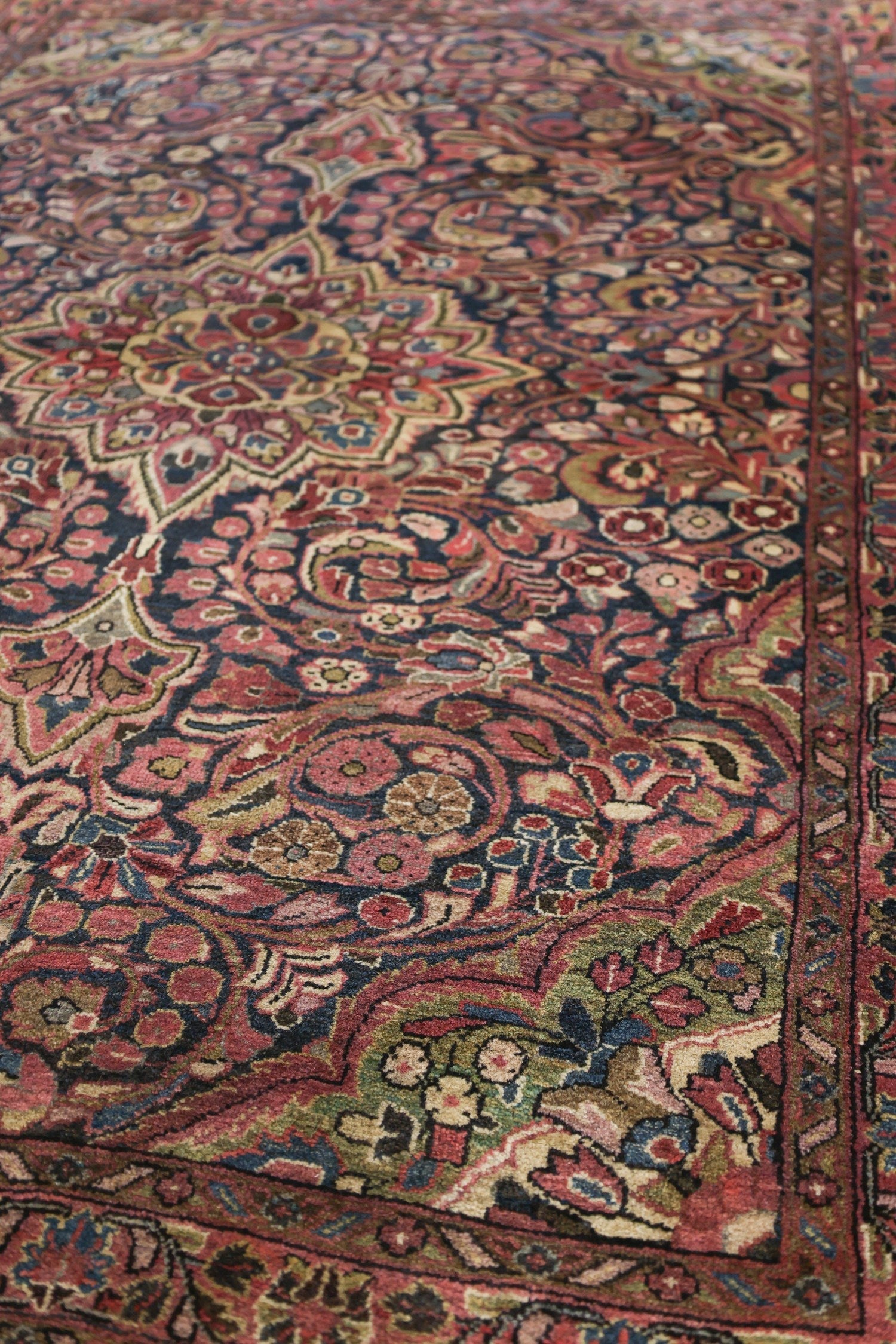 Close-up of antique rug's richly colored, intricate floral pattern.
