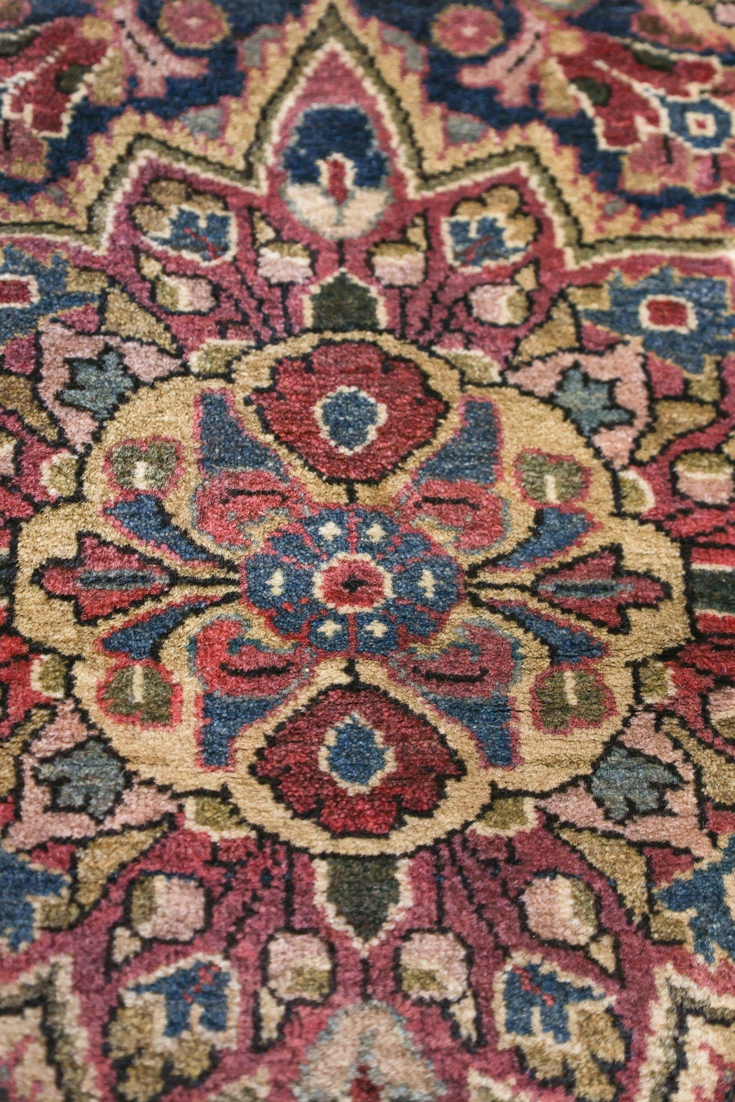 Close-up of a richly colored antique rug, showcasing intricate floral details in red, blue, and beige.
