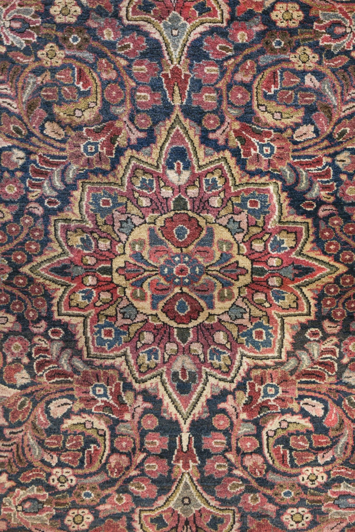 Antique handwoven rug detail: intricate floral medallion in red, beige, and blue tones.
