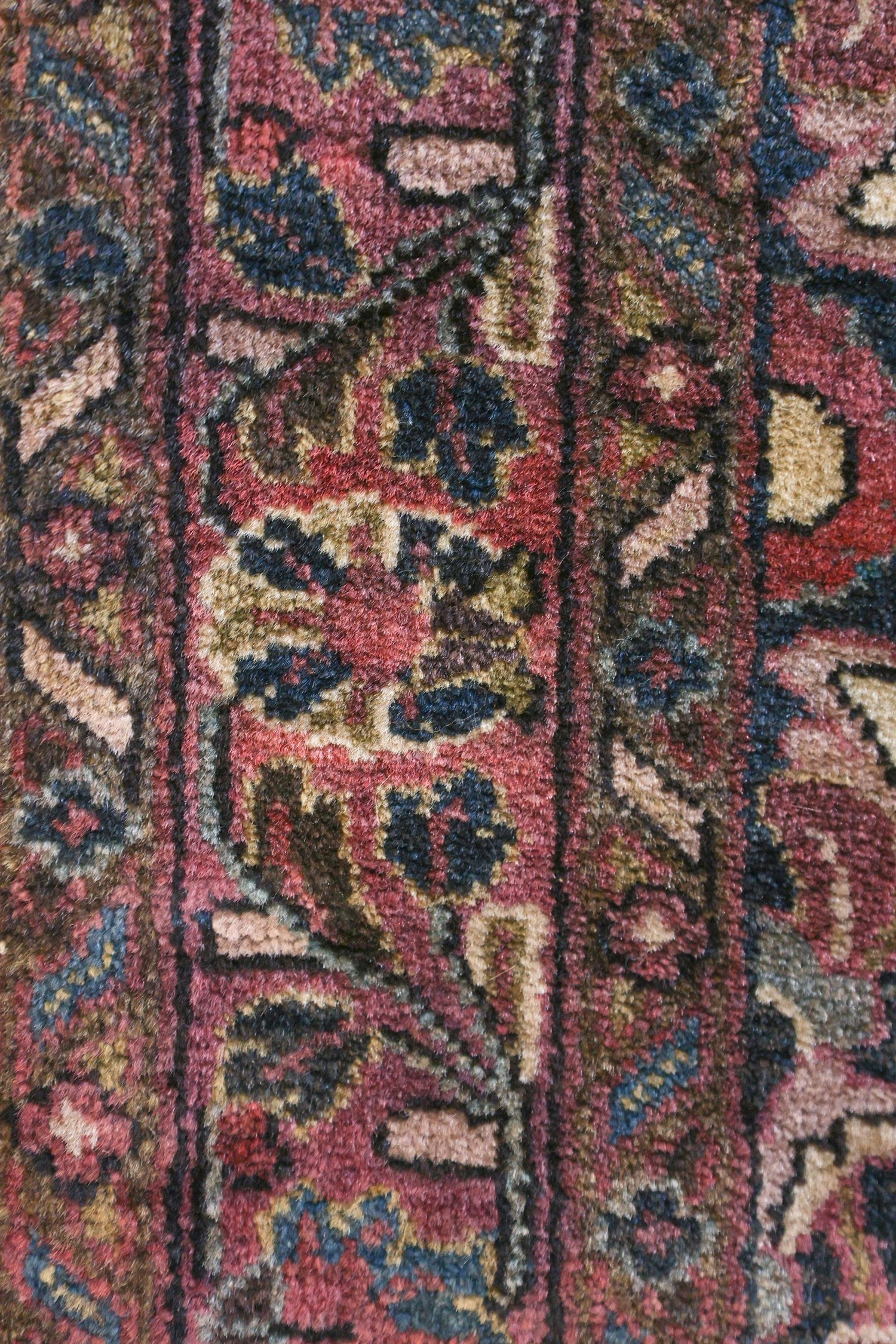 Close-up detail of a richly colored, handwoven rug with intricate floral patterns in deep reds, blues, and browns.
