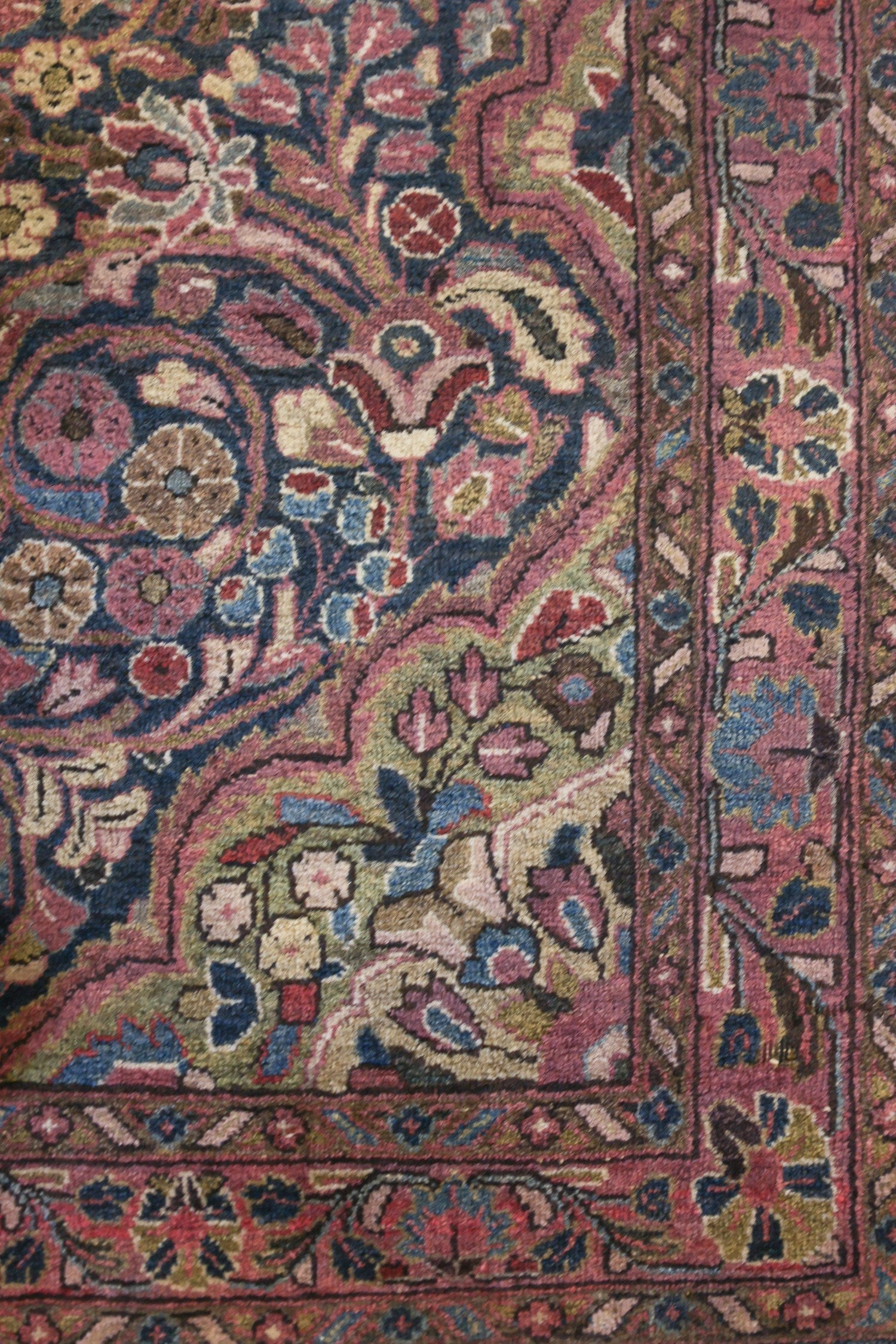 Close-up of a vintage rug's intricate floral pattern in muted pinks, blues, and greens.
