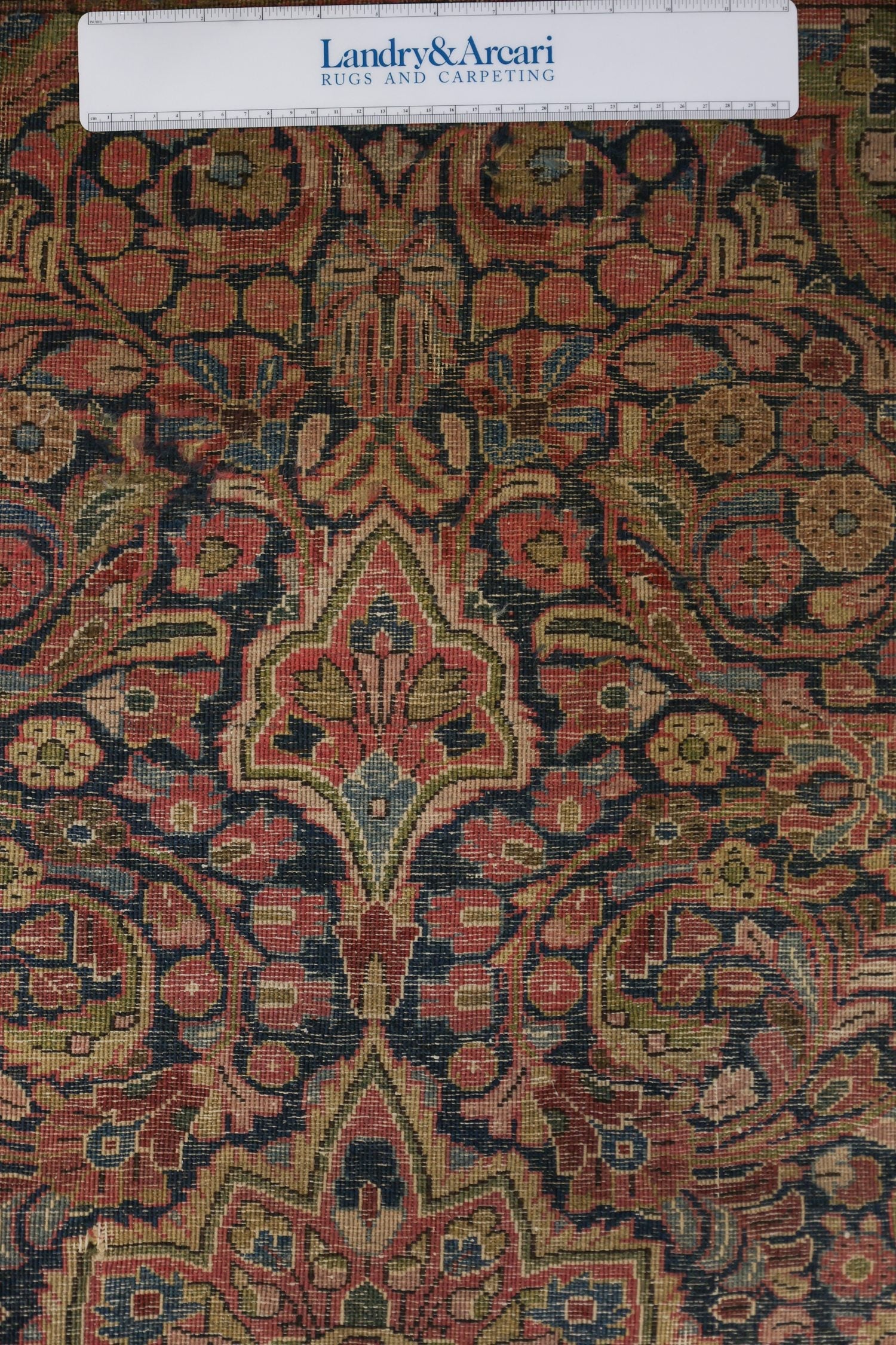 Close-up detail of antique Sarouk rug's intricate, handwoven floral pattern in muted reds and blues.
