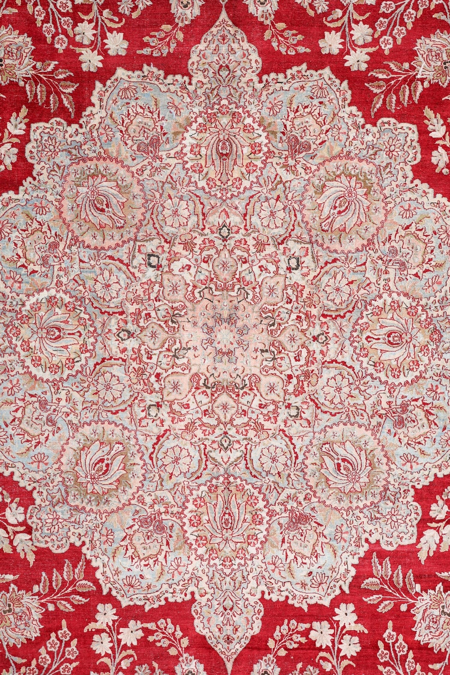 Intricate floral detail on a red antique Kerman rug, handwoven with a traditional design.
