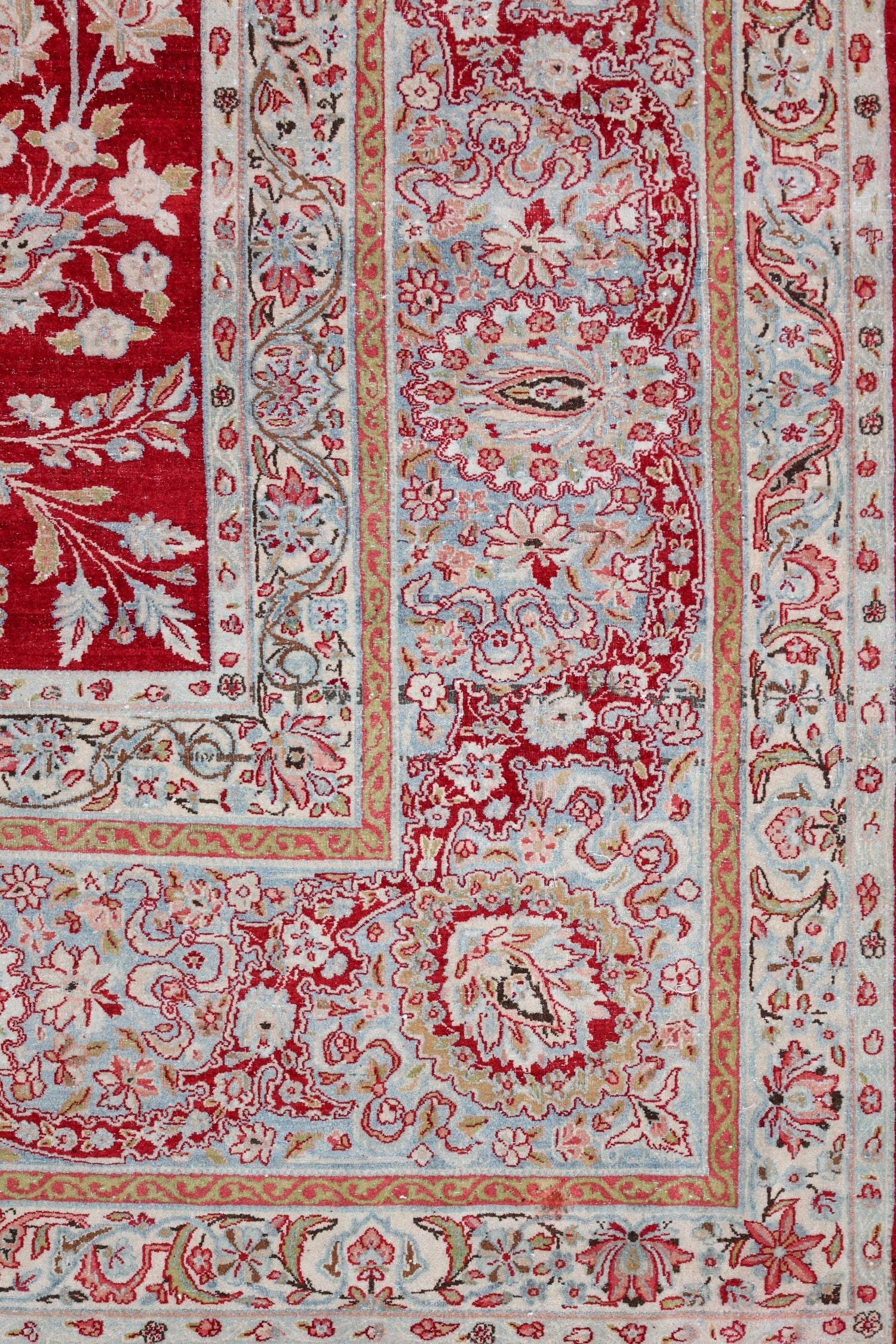 Antique Kerman rug detail: handwoven floral border, red and pale blue hues.
