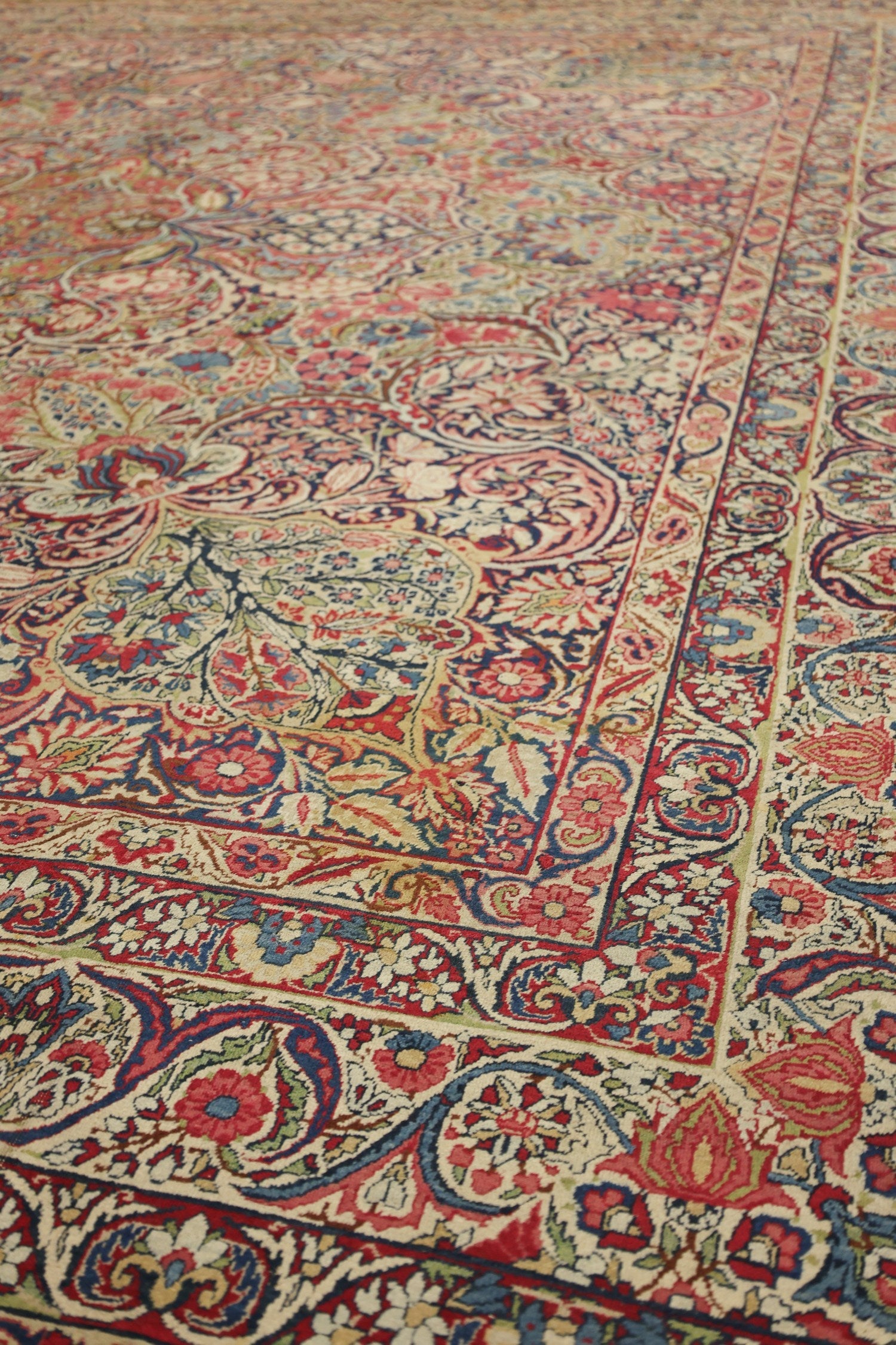 Close-up of antique Kerman rug's intricate floral and paisley pattern, showcasing rich reds, blues, and creams.
