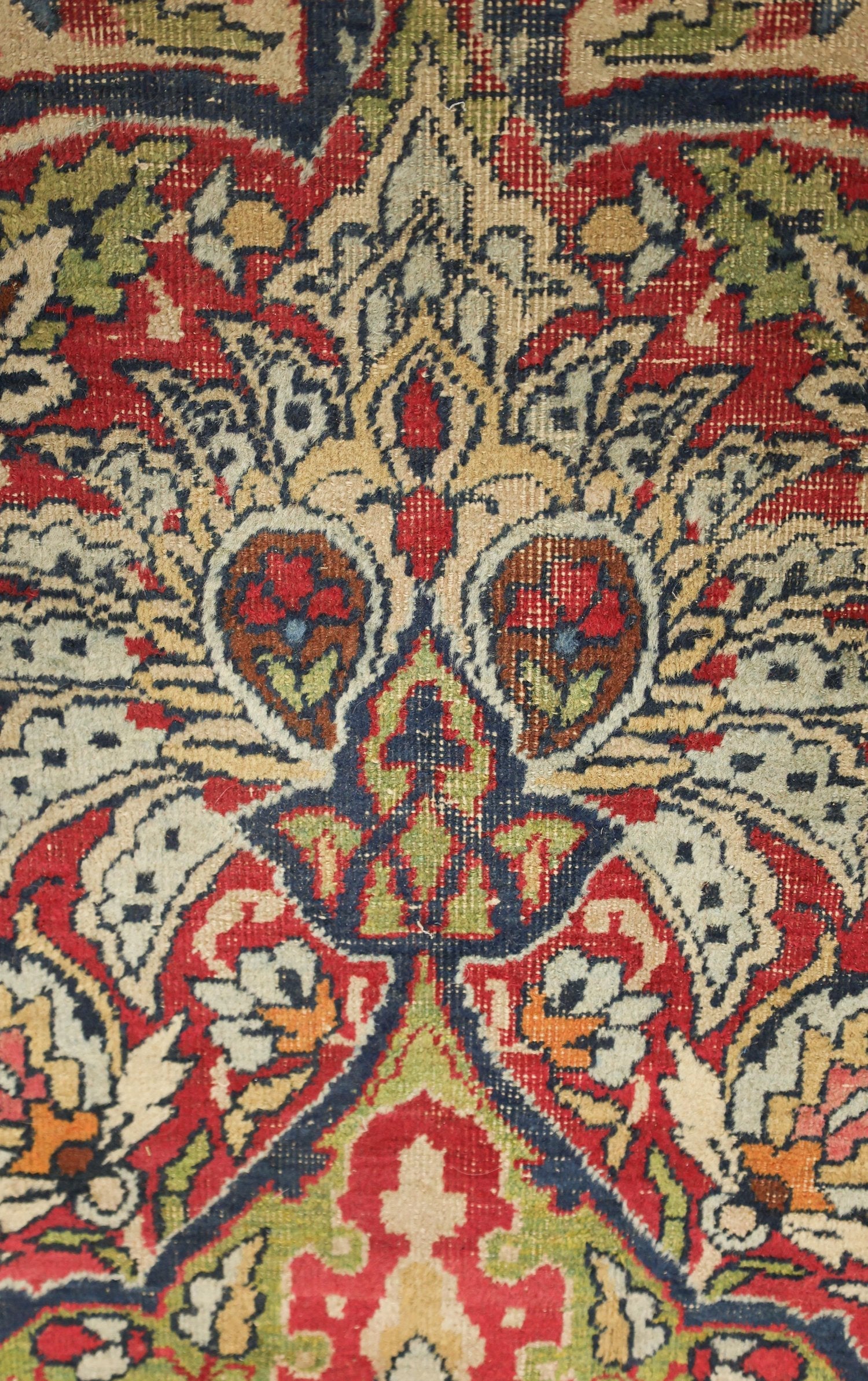 Close-up detail of a richly colored antique Kerman rug, showcasing intricate floral and arabesque patterns in reds, blues, and creams.
