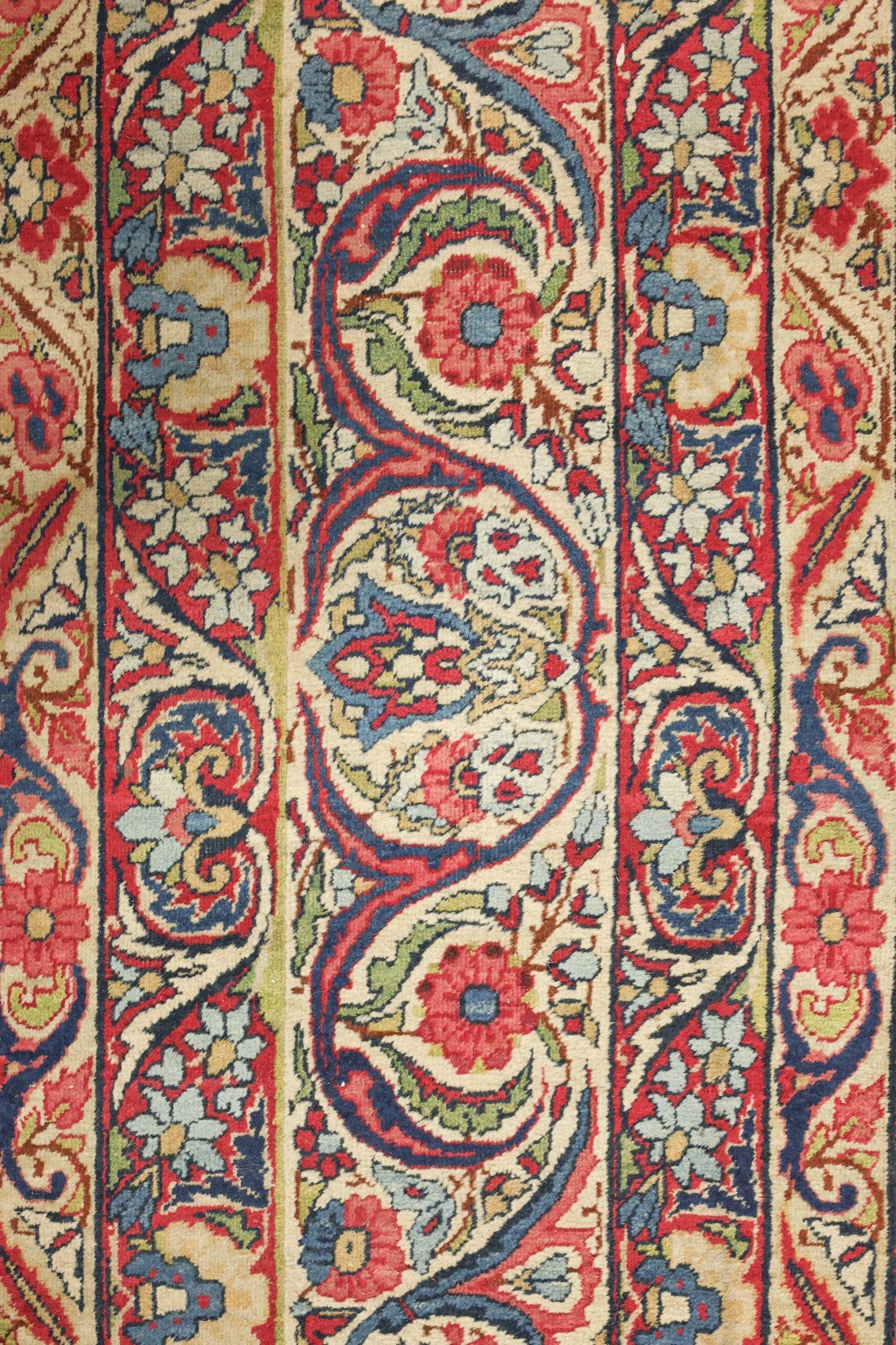 Close-up of antique Kerman rug detail, showcasing intricate floral pattern in red, blue, and cream.
