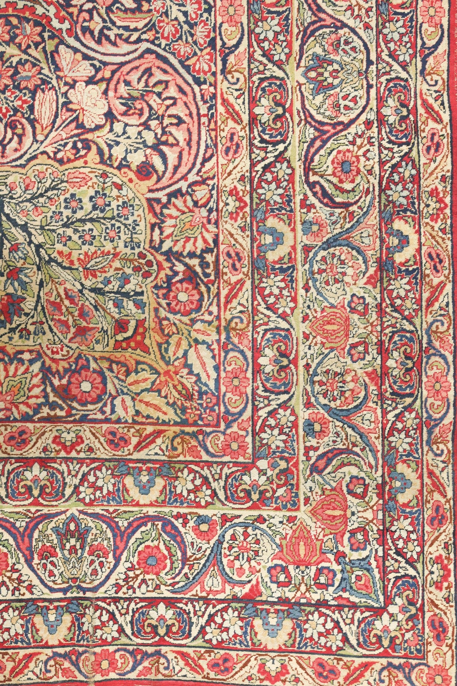 Detail of antique Kerman rug, showcasing a floral and paisley design in red, blue, and cream.
