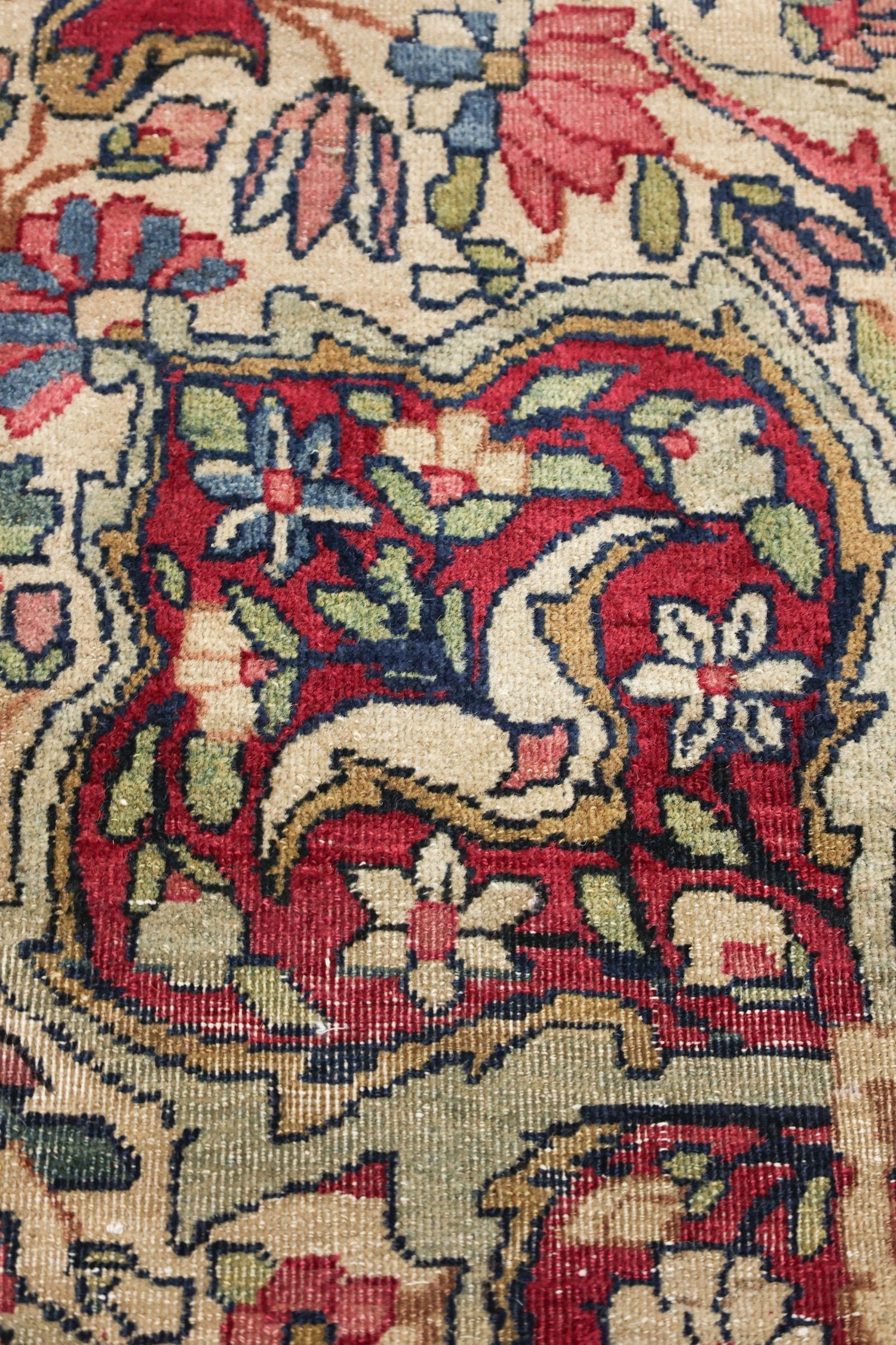 Close-up of antique rug detail: intricate floral pattern in red, beige, and blue.
